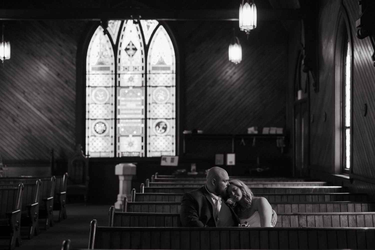 Black and white photo of a couple sharing an intimate moment in a historic church with stunning stained glass windows.