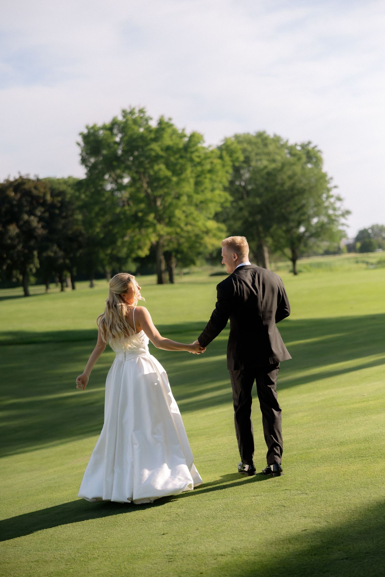 Bride and groom walking hand in hand across a lush green golf course on their wedding day.