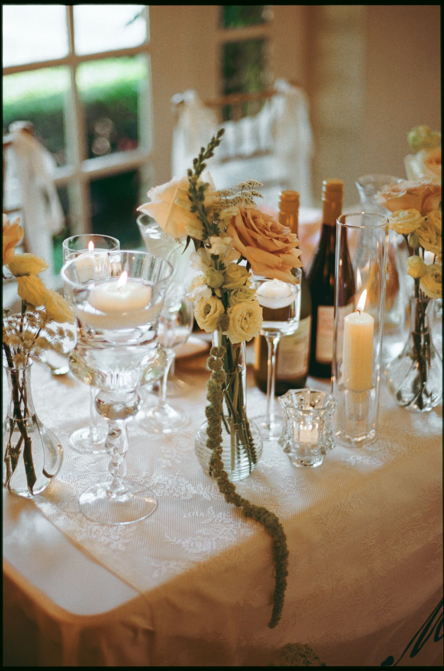 Elegant wedding table setting with white roses, candles, and crystal glassware on a lace tablecloth.