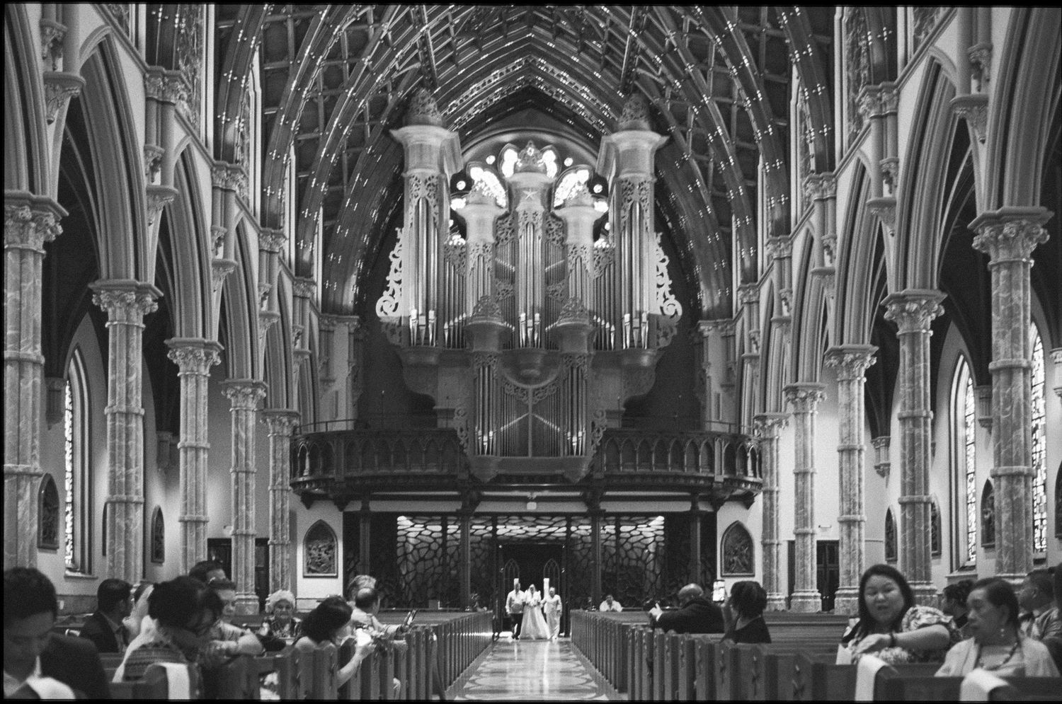 Black and white photo of a grand cathedral interior with ornate arches, pipe organ, and congregation seated in pews.