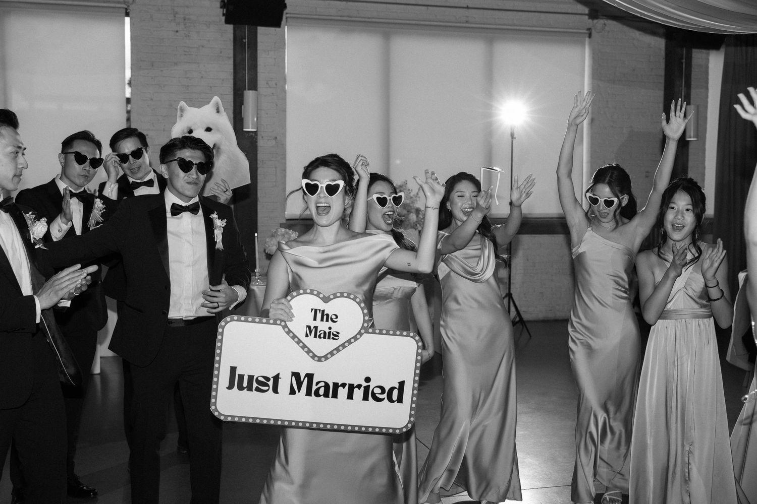Bride holds Just Married sign surrounded by bridesmaids and groomsmen in black and white wedding photo.