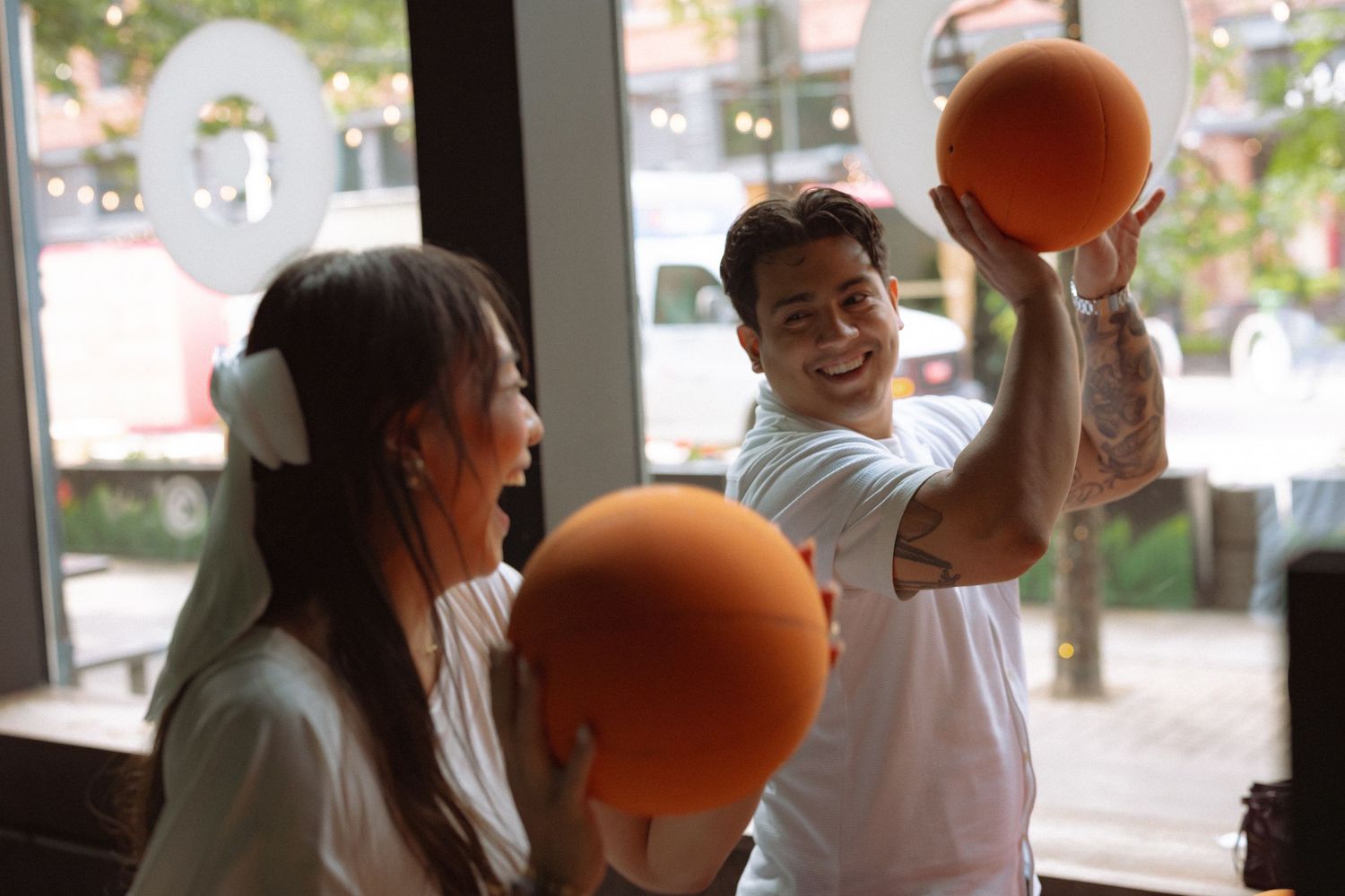 Two people smiling and holding orange balls indoors, enjoying a fun activity together.