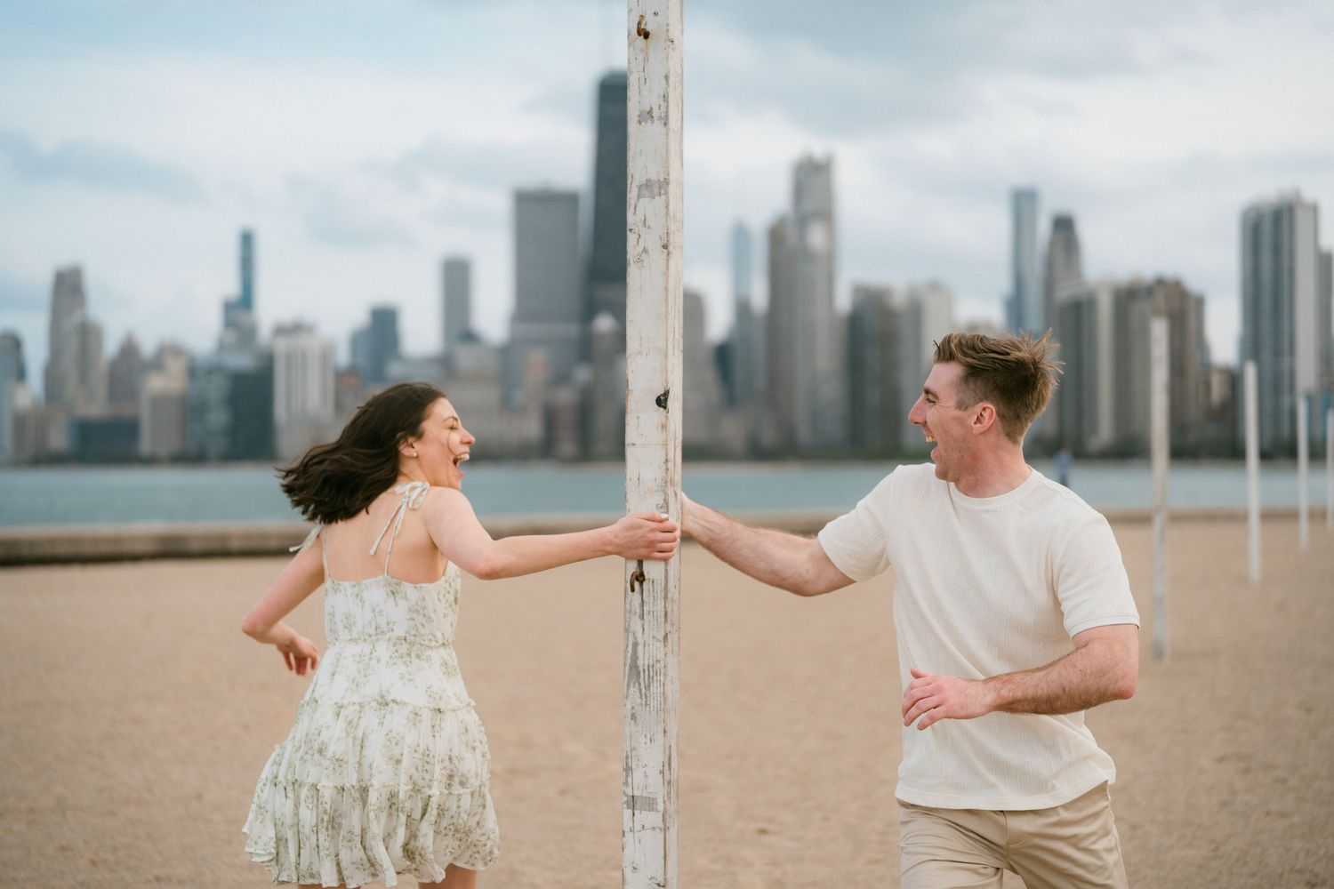 Playful couple laughing around a beach post with Chicago city skyline in background.