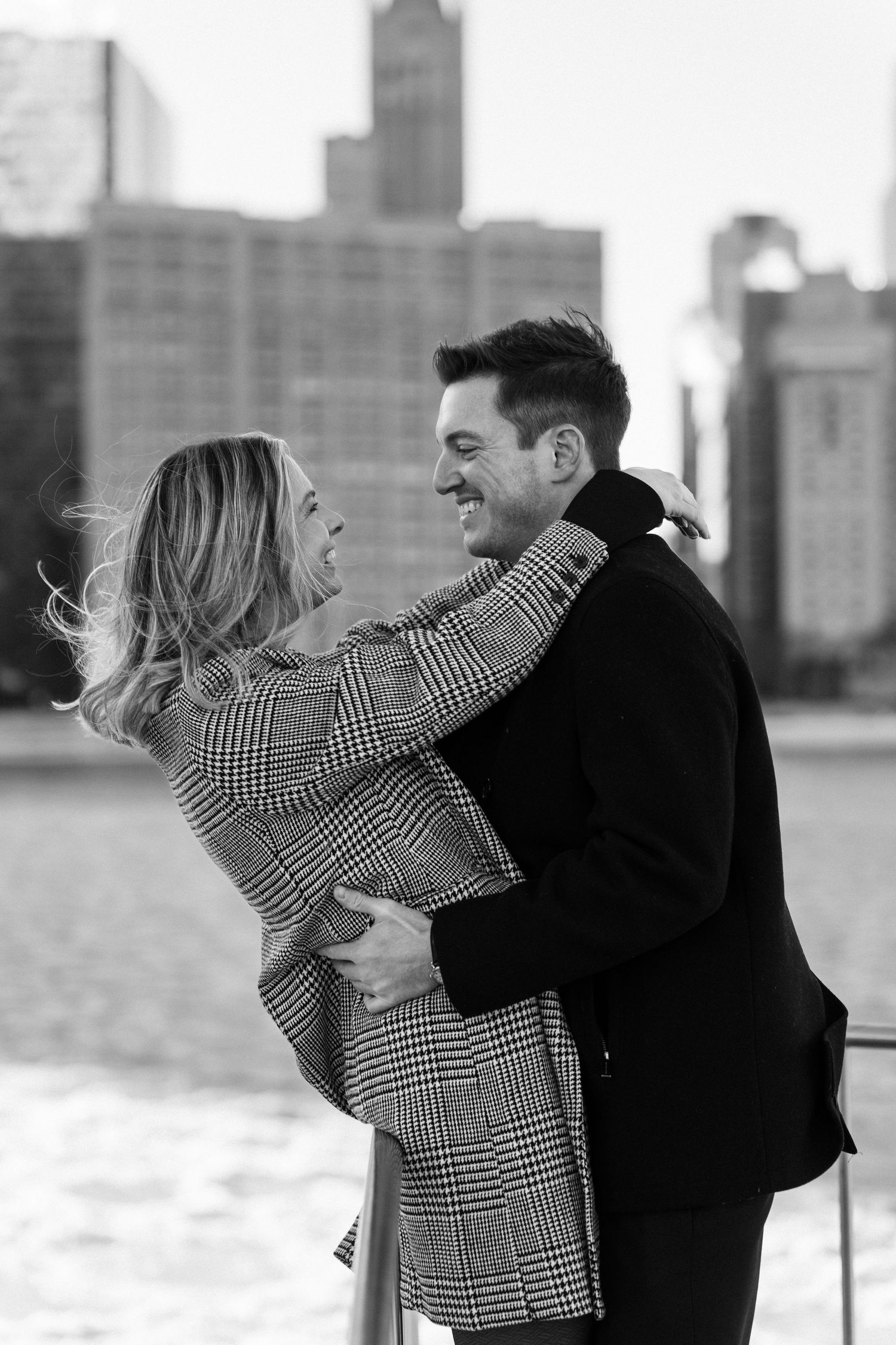 Black and white photo of couple hugging and laughing by Chicago waterfront.