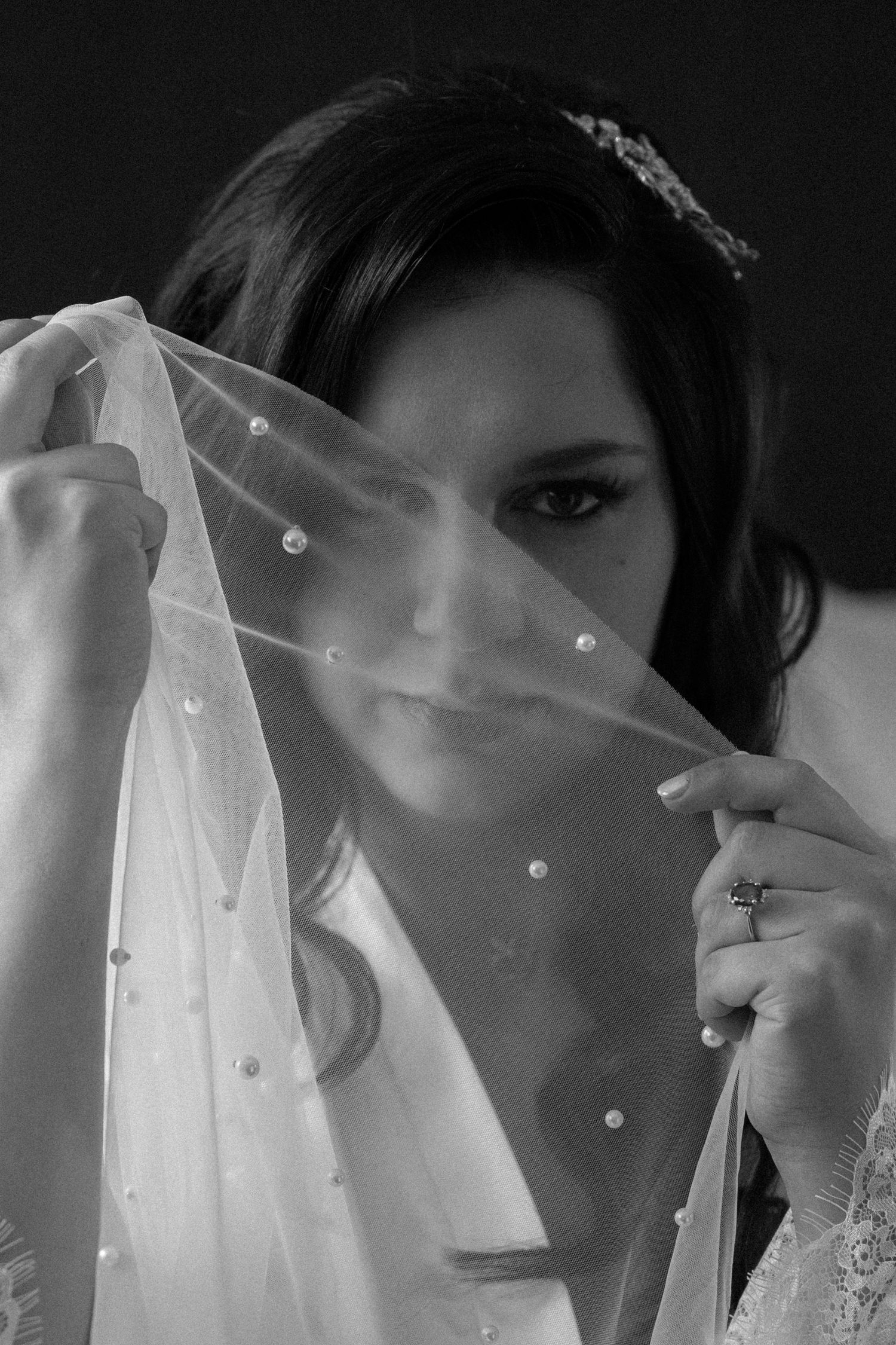 Elegant black and white portrait of a bride holding her pearl-embellished veil over her face.