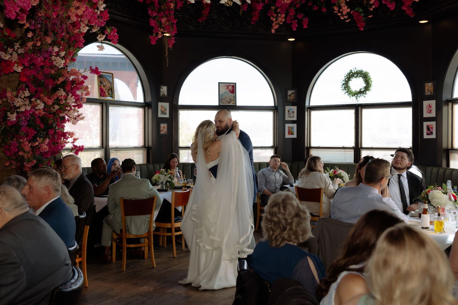 Bride and groom share first dance kiss at elegant wedding reception with floral decor and guests seated at tables.