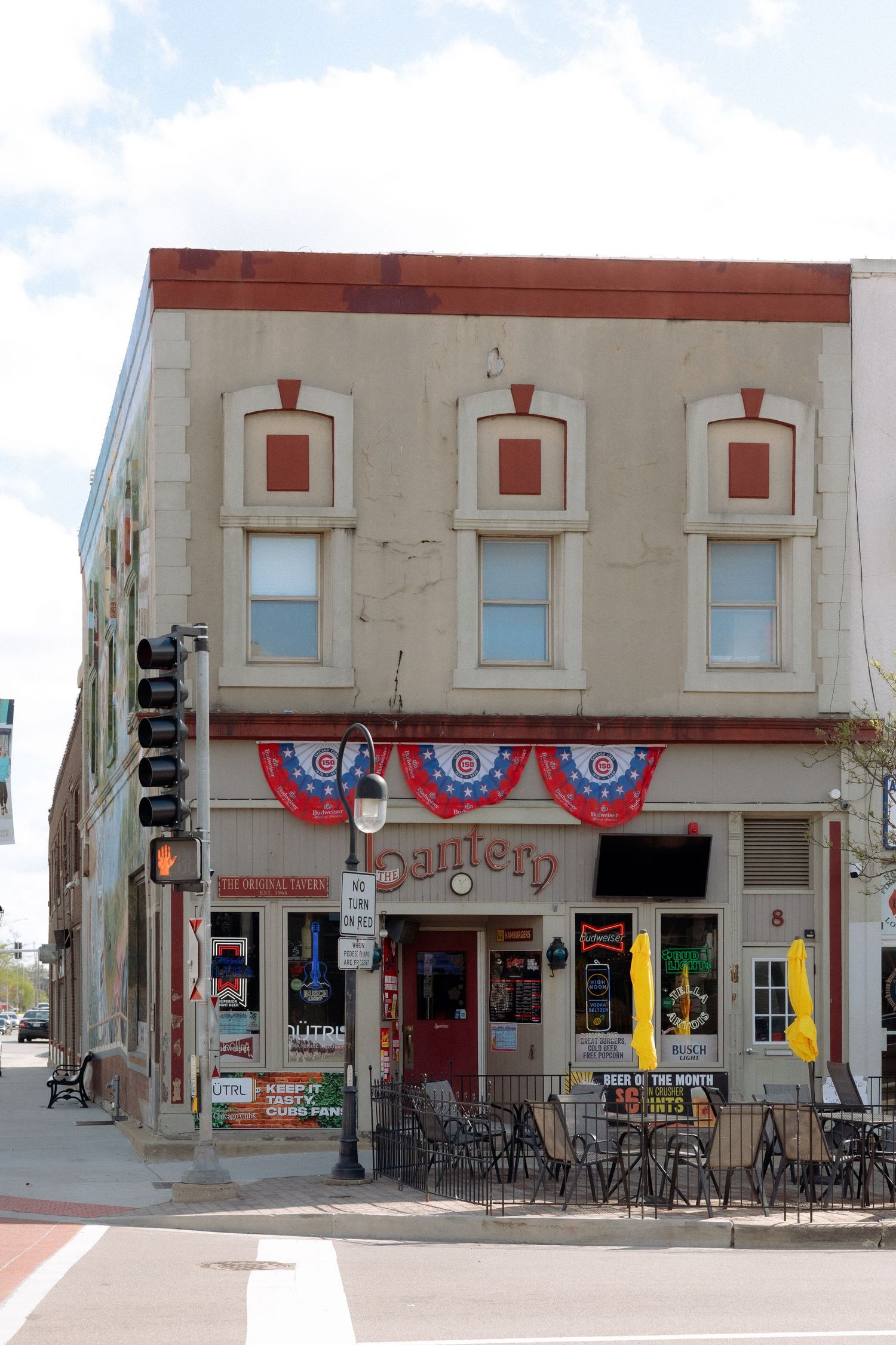 Corner bar called Lantern with patriotic bunting decorations, outdoor seating, and a traffic light on a small-town street.