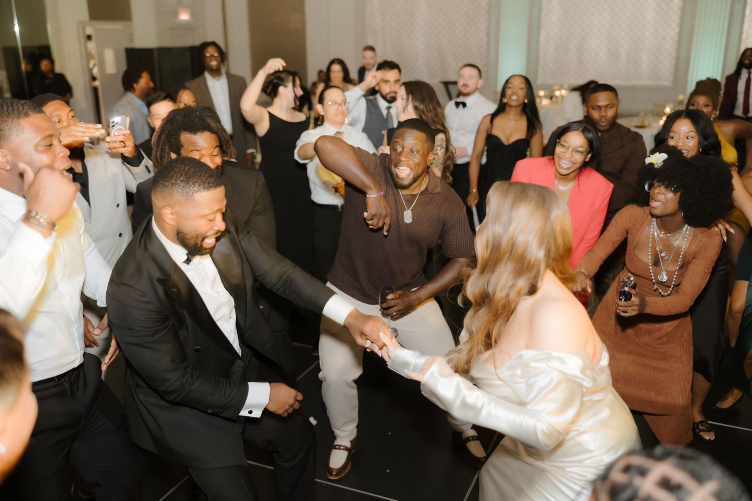 Bride and groom dancing joyfully with guests at a lively wedding reception celebration.