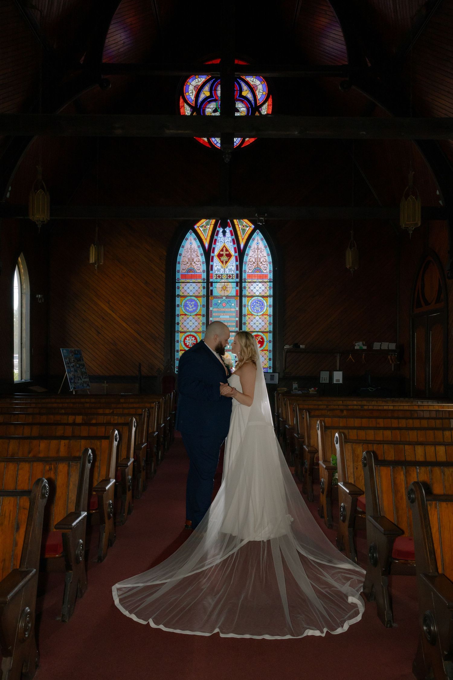 Bride and groom share a romantic moment at the altar of a wooden church with stunning stained glass windows.