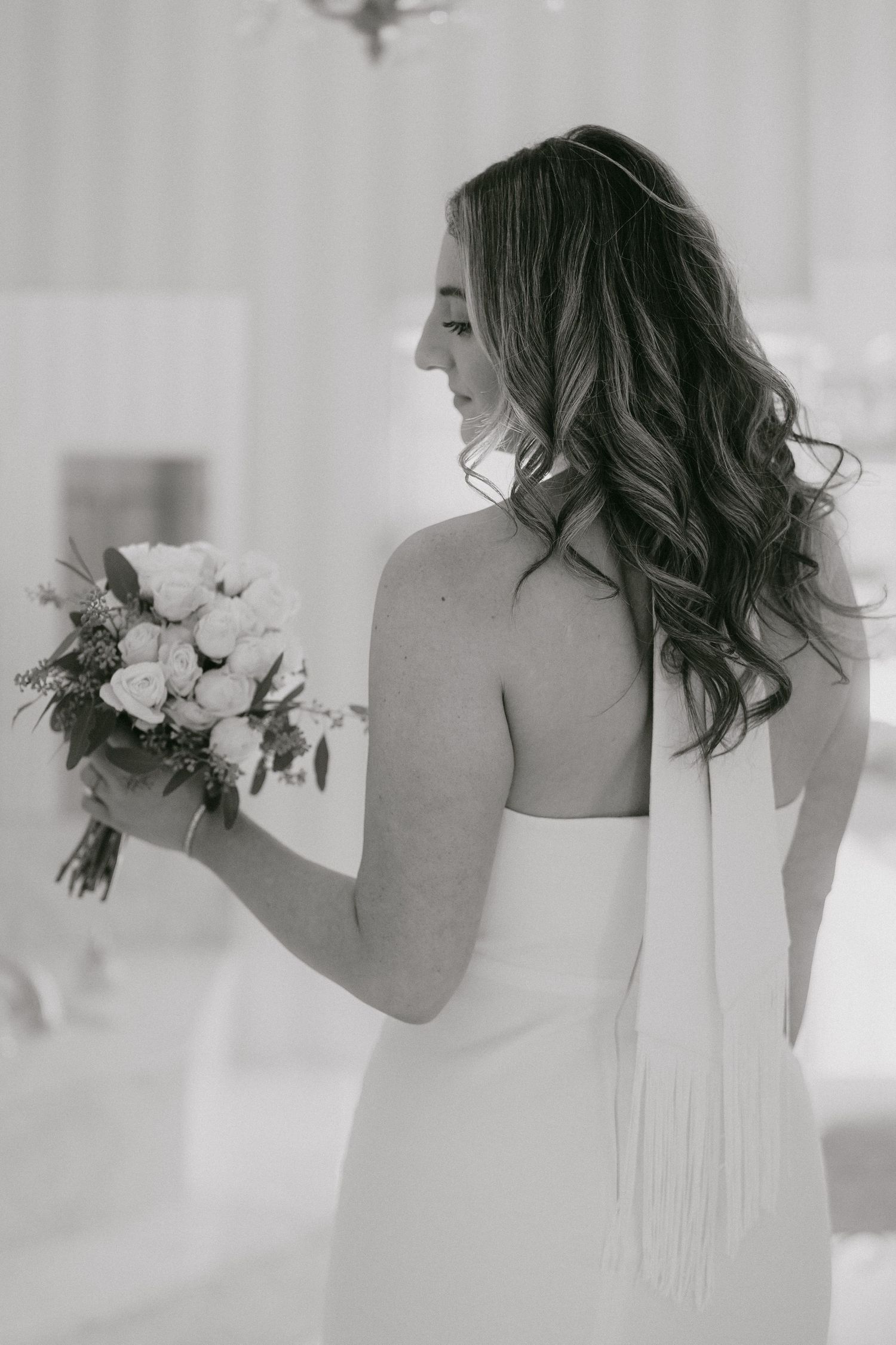 Black and white photo of bride in strapless gown holding white rose bouquet looking away.