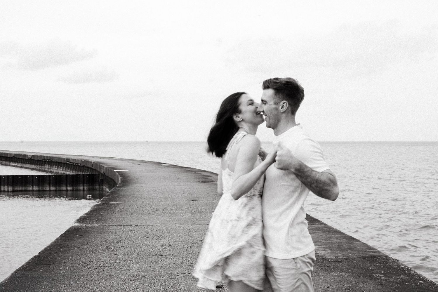 Black and white photo of a romantic couple embracing on a waterfront pier.