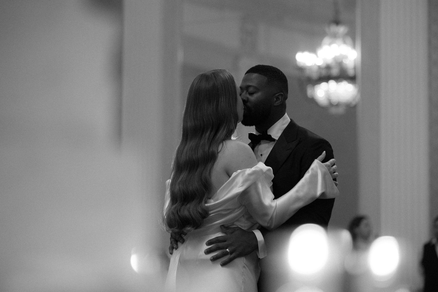 Black and white photo of a couple sharing their first dance at an elegant wedding reception.