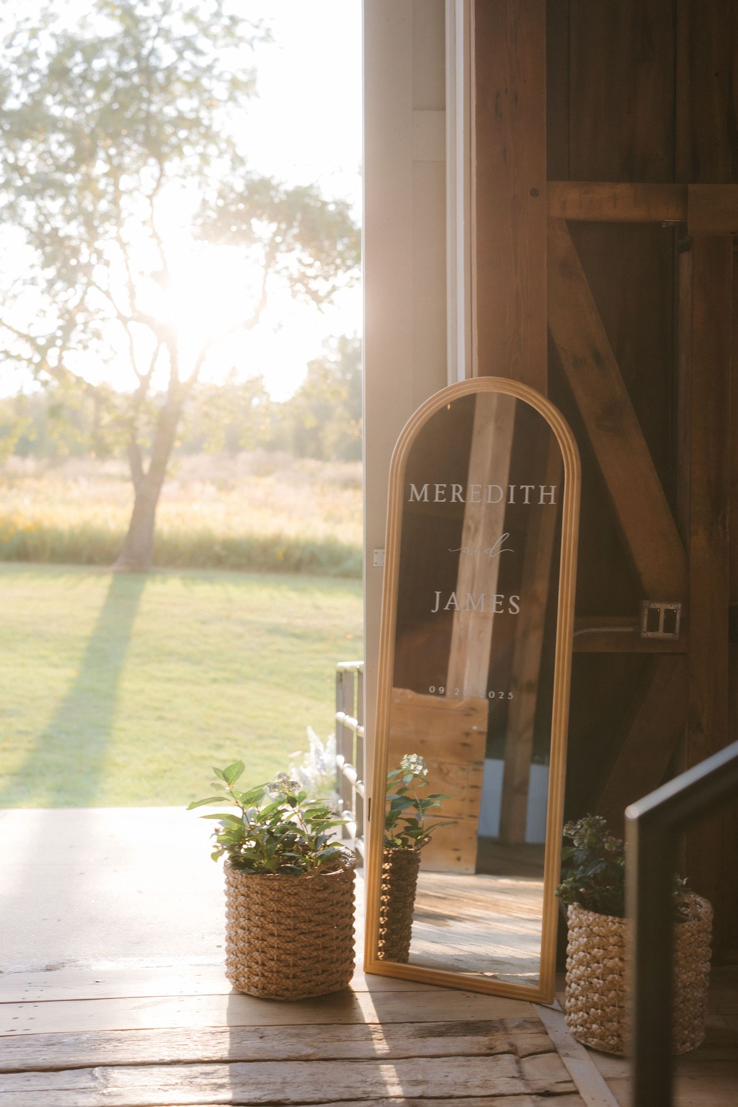 Gold arched mirror with Meredith and James wedding signage in a sunlit barn doorway.
