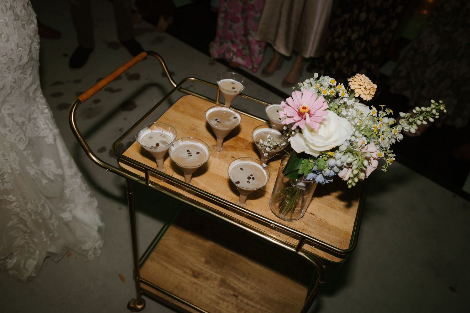 Gold bar cart with floral centerpiece and dessert cups at an elegant wedding reception.