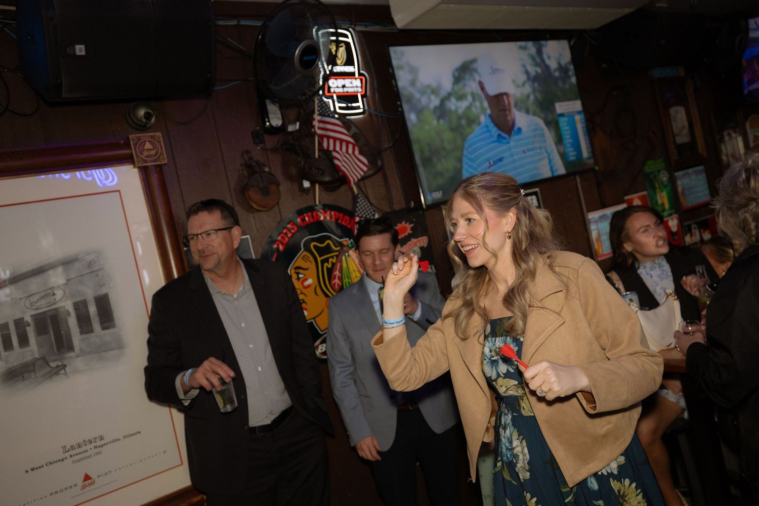People socializing at a lively bar event with a golf broadcast on TV in the background.