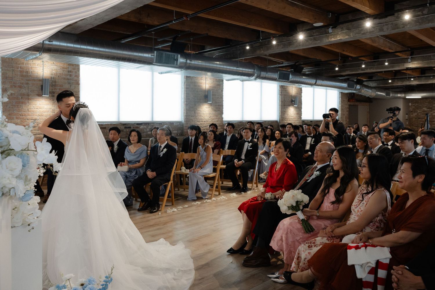 Bride and groom stand at the altar during an elegant indoor wedding ceremony with guests seated in rows.