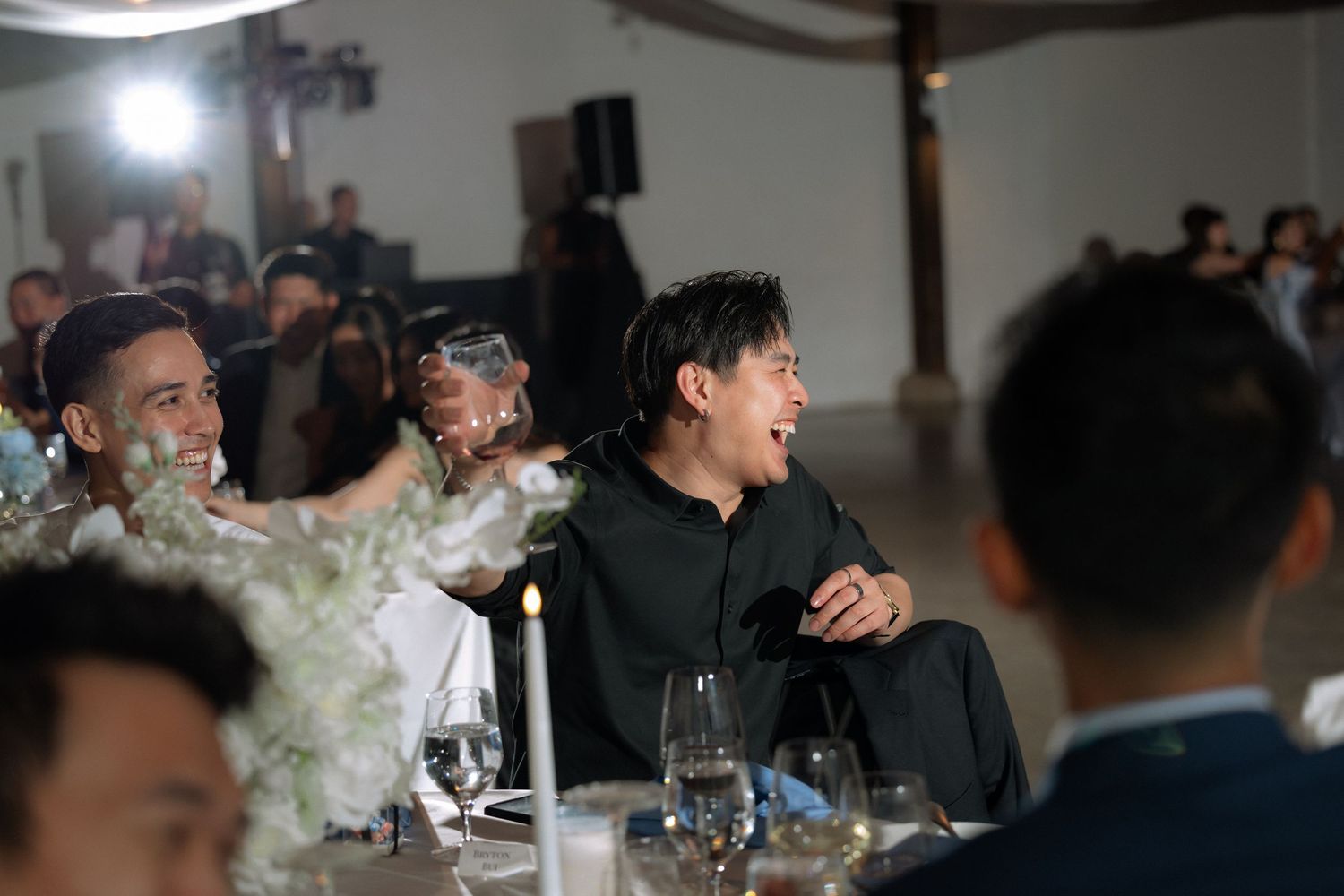 Guests laughing and enjoying conversation at elegantly set wedding reception dinner table.