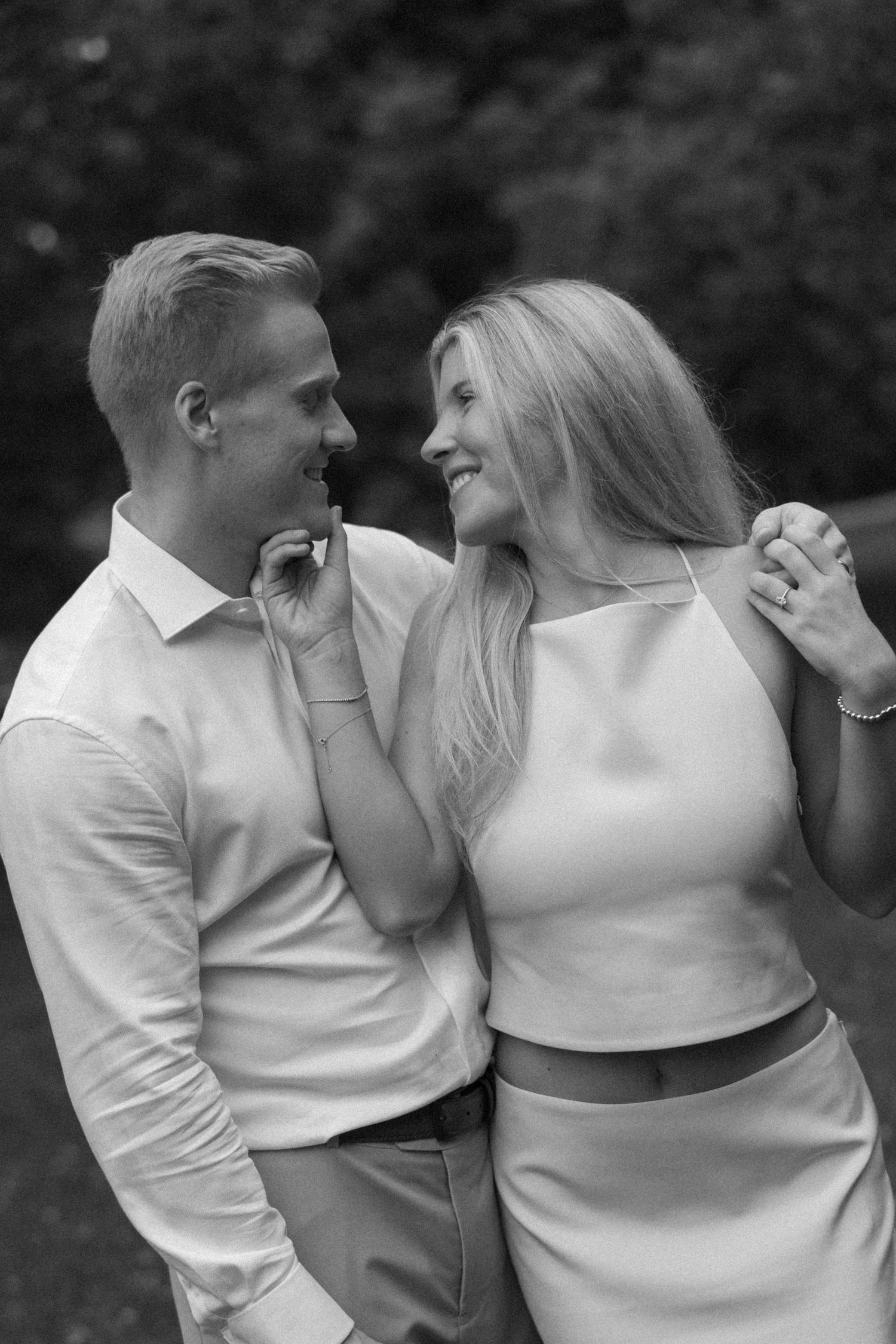 Black and white photo of a smiling couple embracing outdoors, the woman in a crop top and the man in a white shirt.