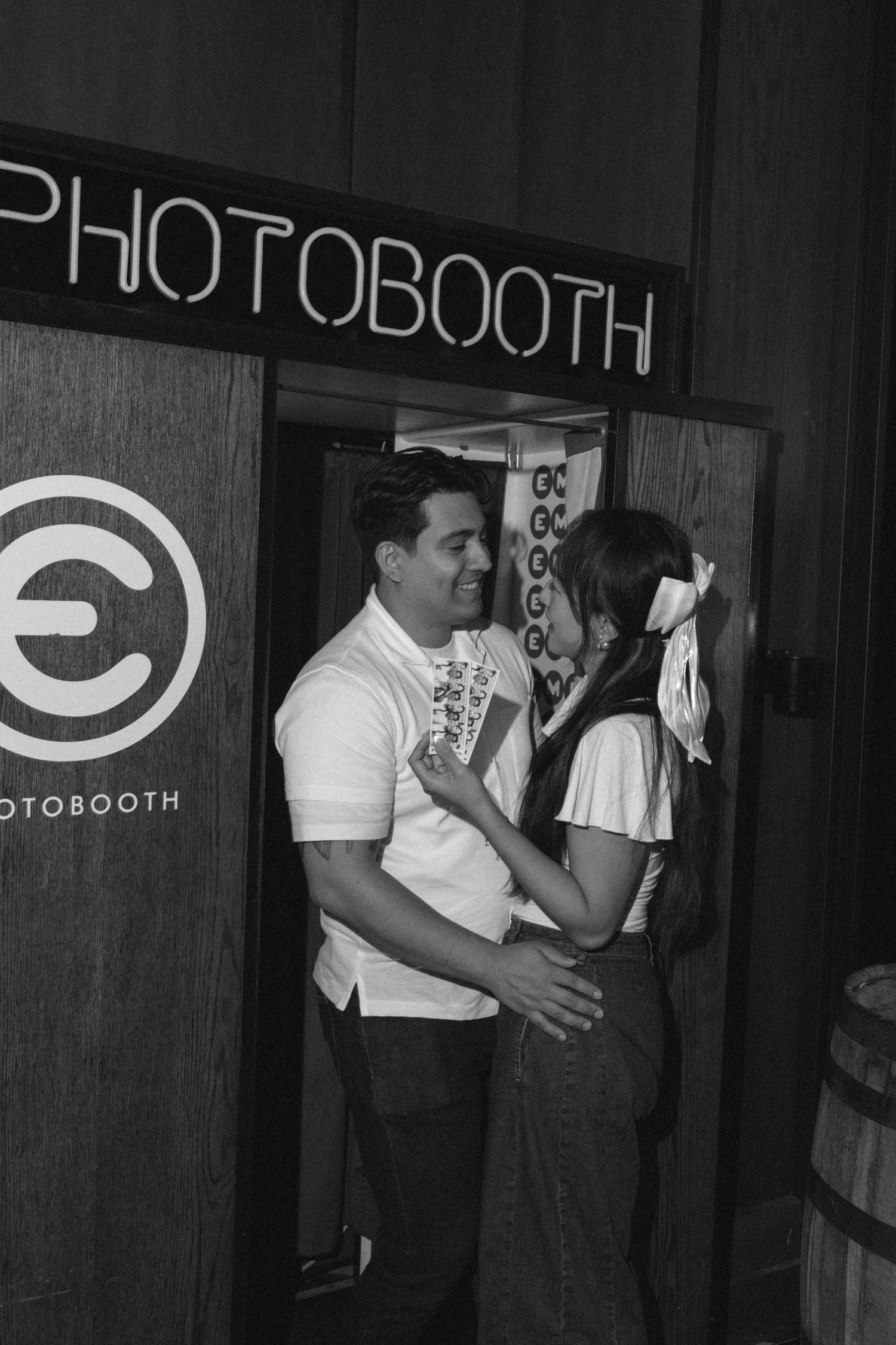 Black and white photo of couple embracing and smiling outside a vintage photobooth.