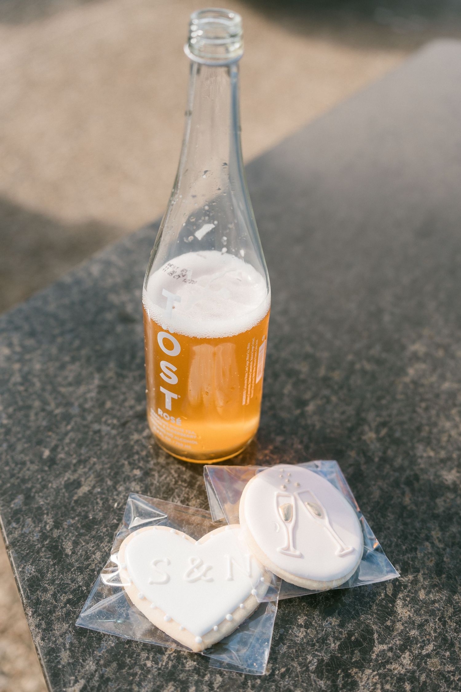Bottle of OST sparkling cider beside two custom engagement cookies with initials S and I.