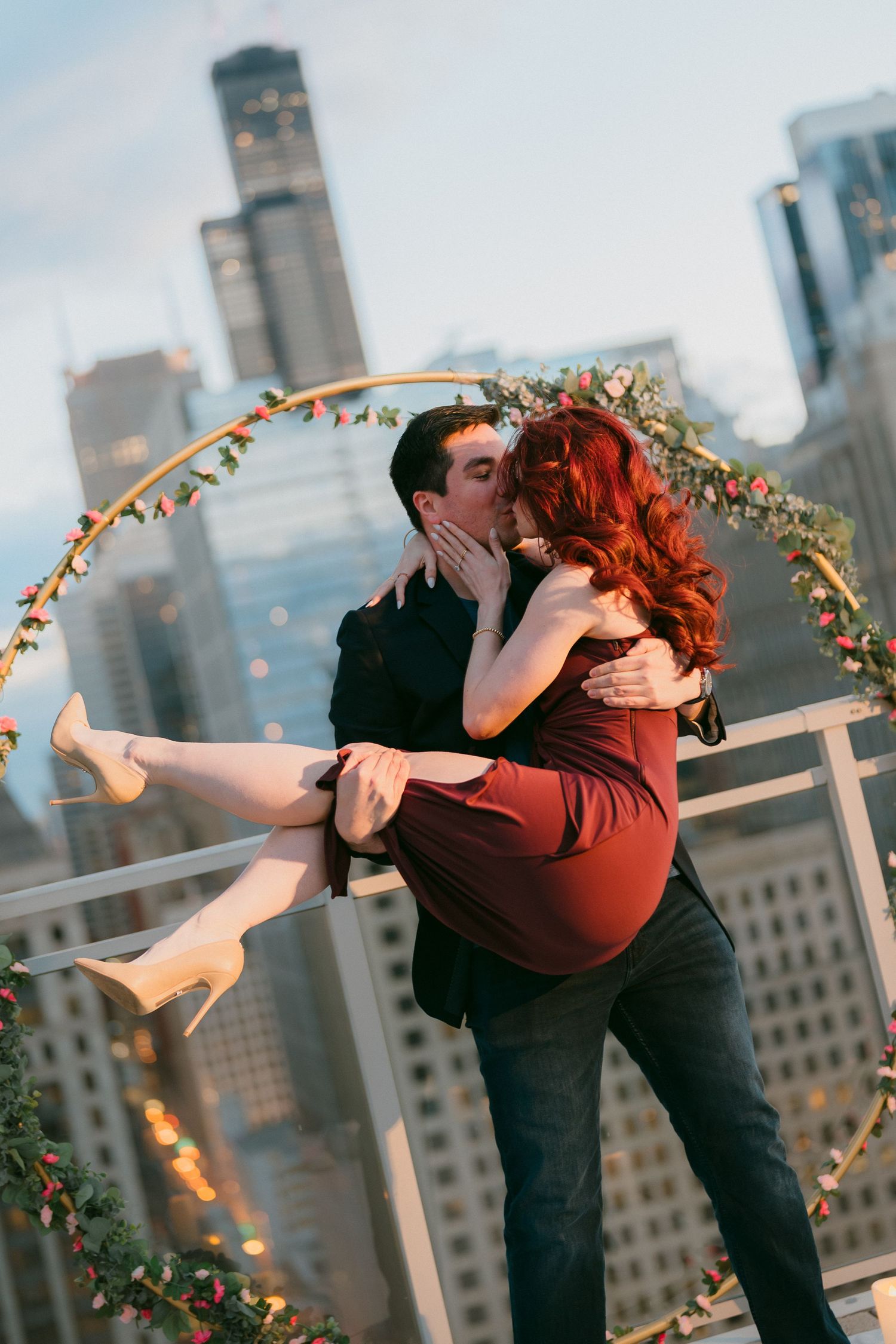 Couple kissing on Chicago rooftop with floral hoop arch and city skyline backdrop.
