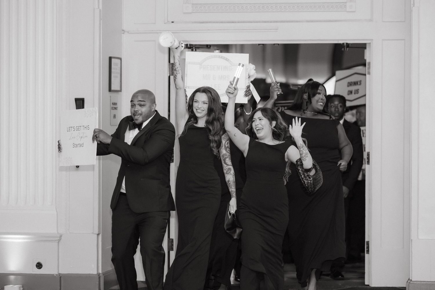 Group of elegantly dressed people in black attire walking through a doorway at a formal event.