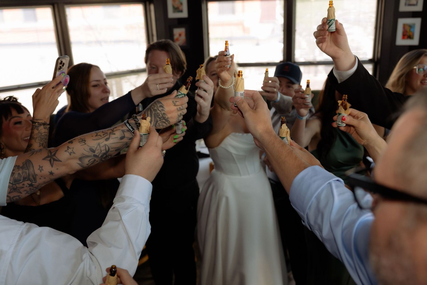 Wedding guests raising shot glasses in a celebratory toast with the bride at an indoor venue.