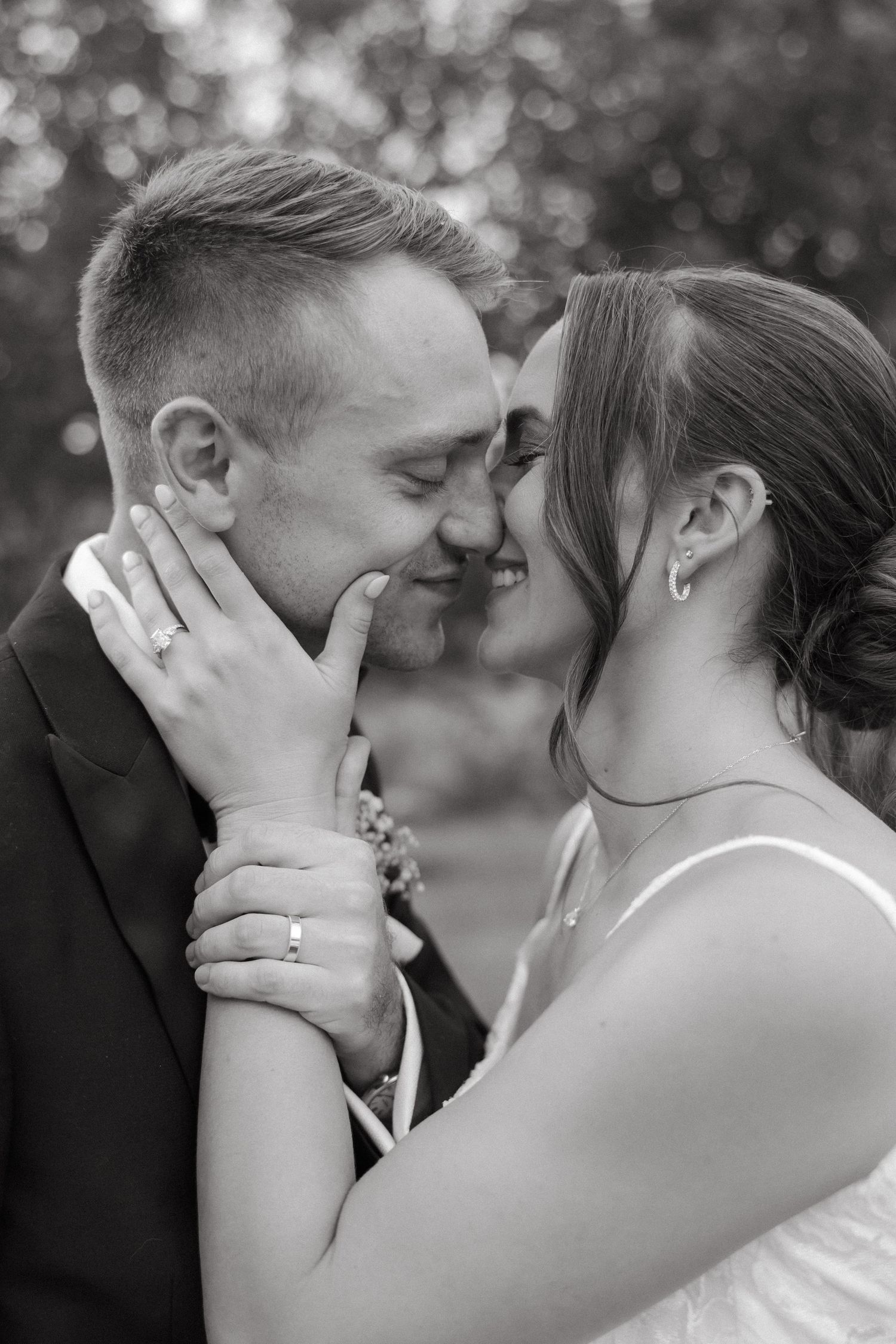 Black and white close-up of bride cradling groom's face as they share an intimate moment, wedding rings visible.