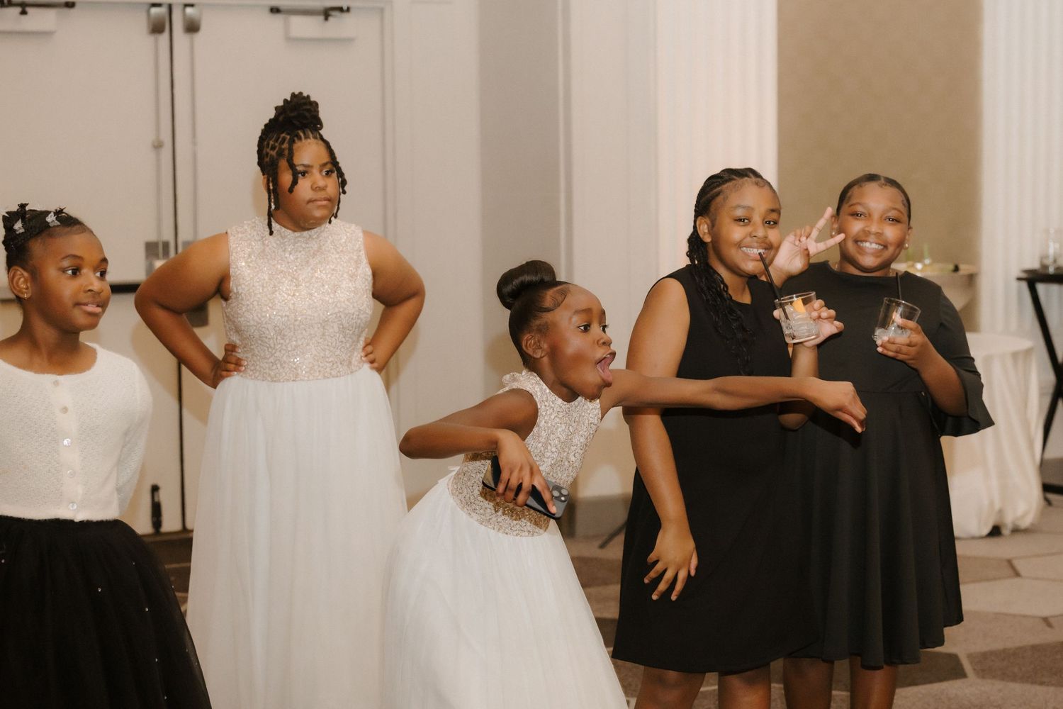 Young girls in black and white dresses posing and dancing together at a wedding reception celebration.