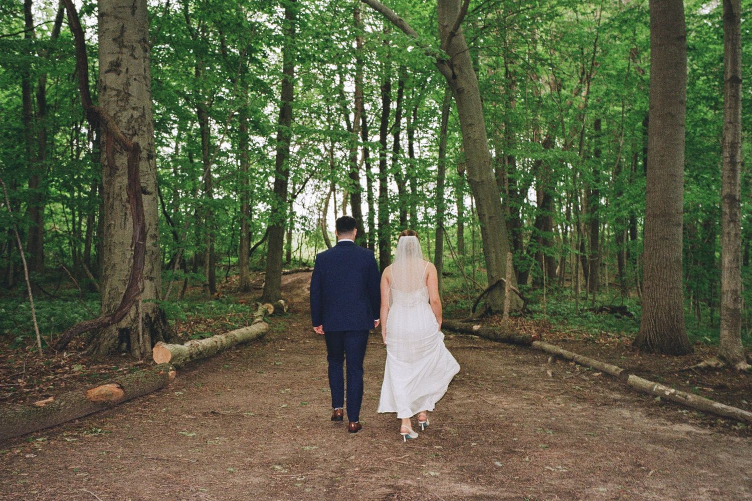 Bride and groom walking hand in hand through a lush green forest on their wedding day.