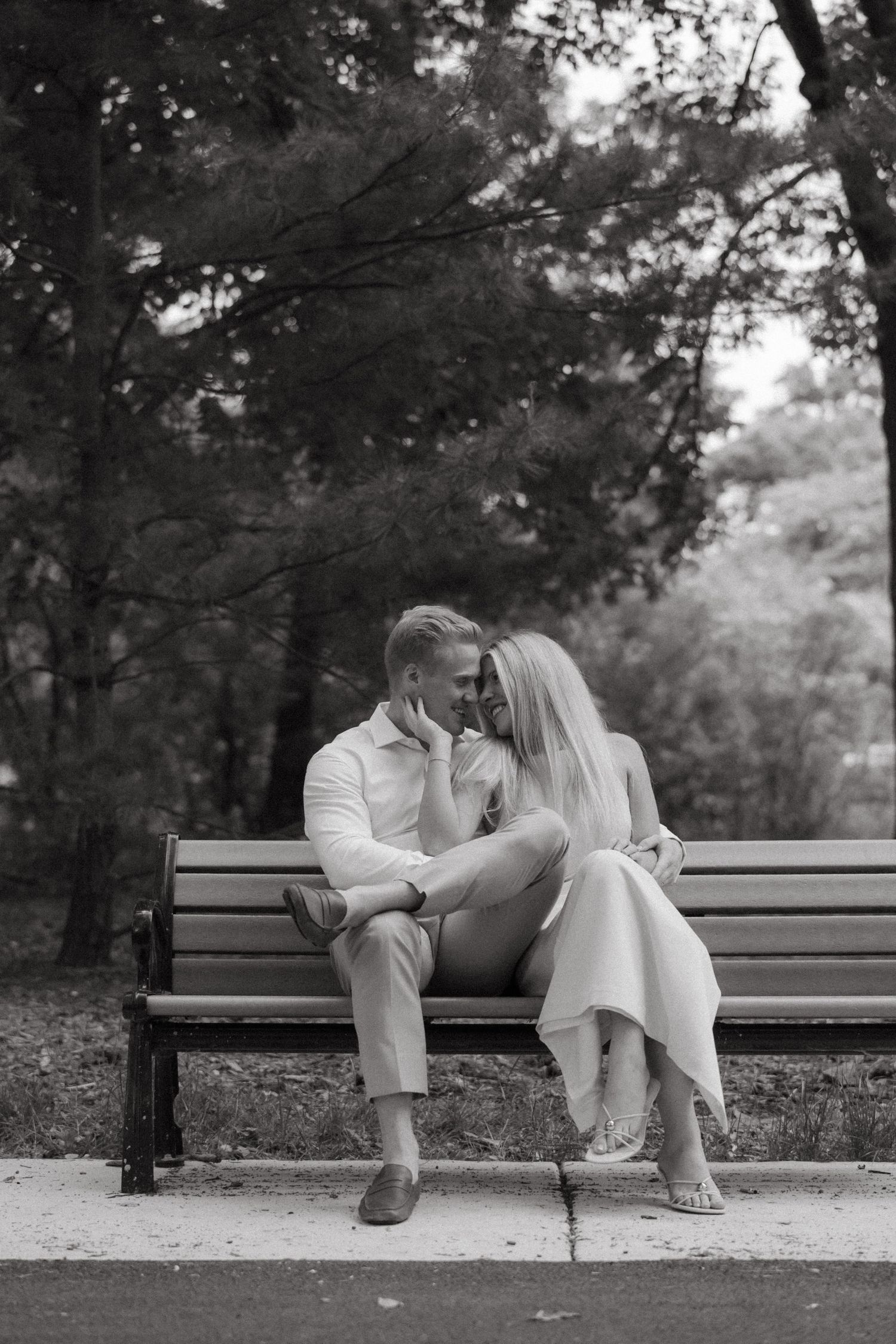 Romantic couple sitting close on a park bench, sharing an intimate moment face to face in black and white photo.