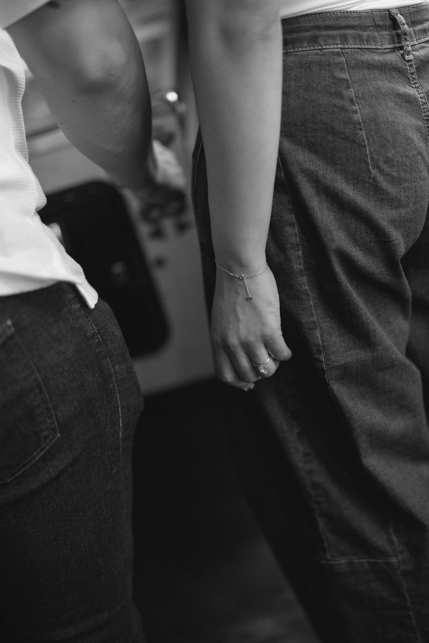 Black and white photo of couple holding hands, woman wearing delicate bracelet, both in jeans.