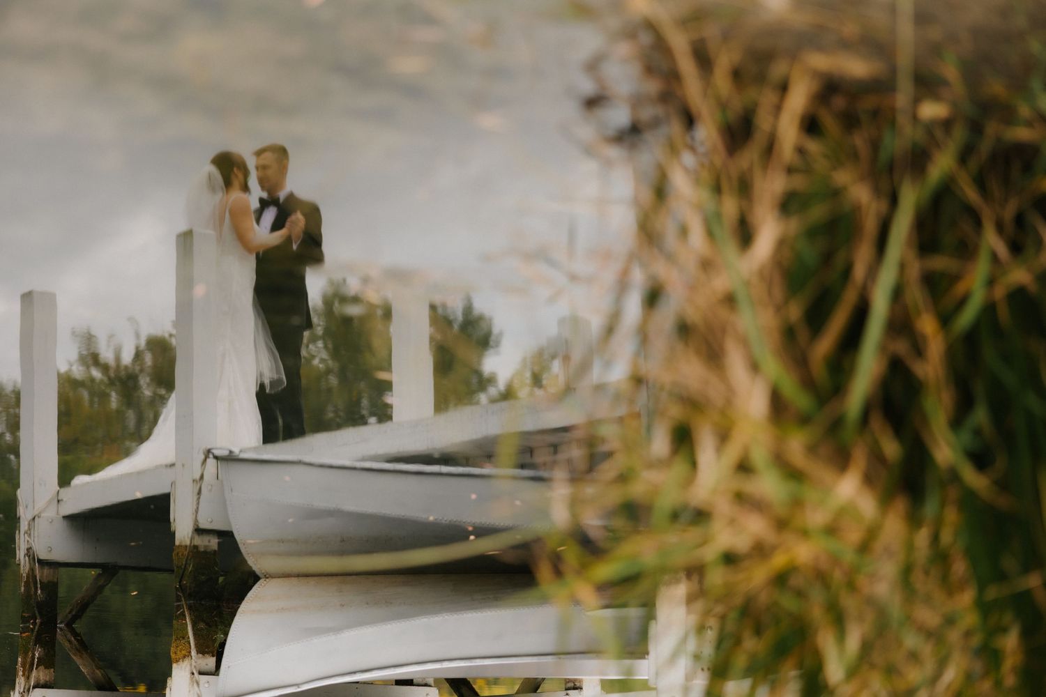 Dreamy reflection of bride and groom kissing on a wooden dock near a calm lake.