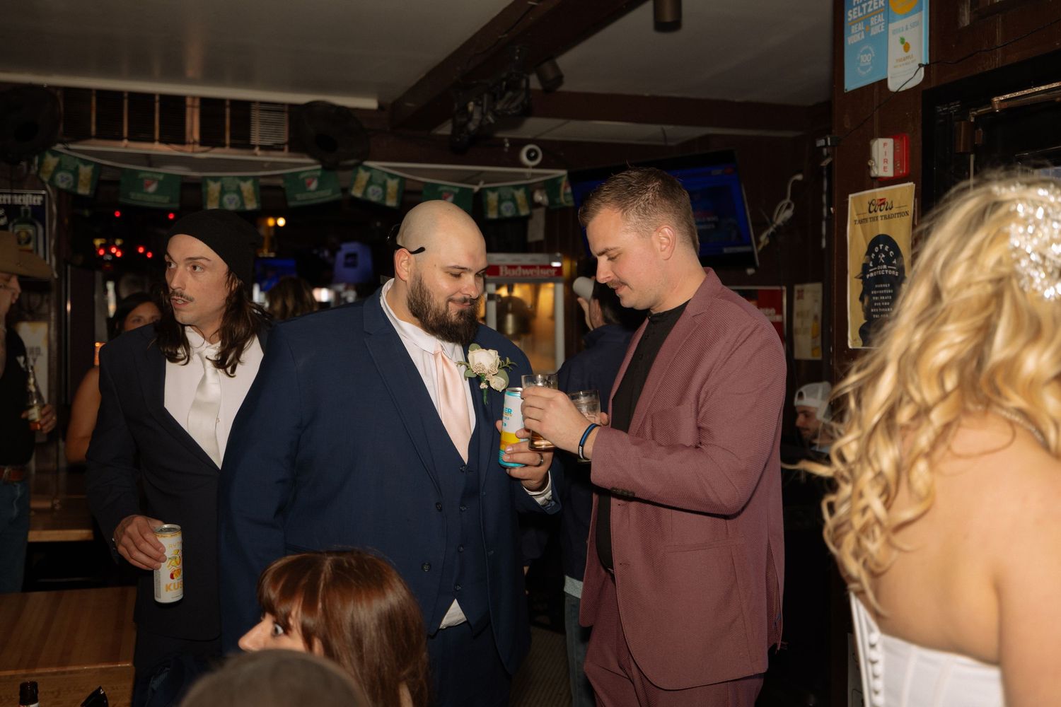 Groom in blue suit toasting drinks with guest in burgundy jacket at wedding reception.