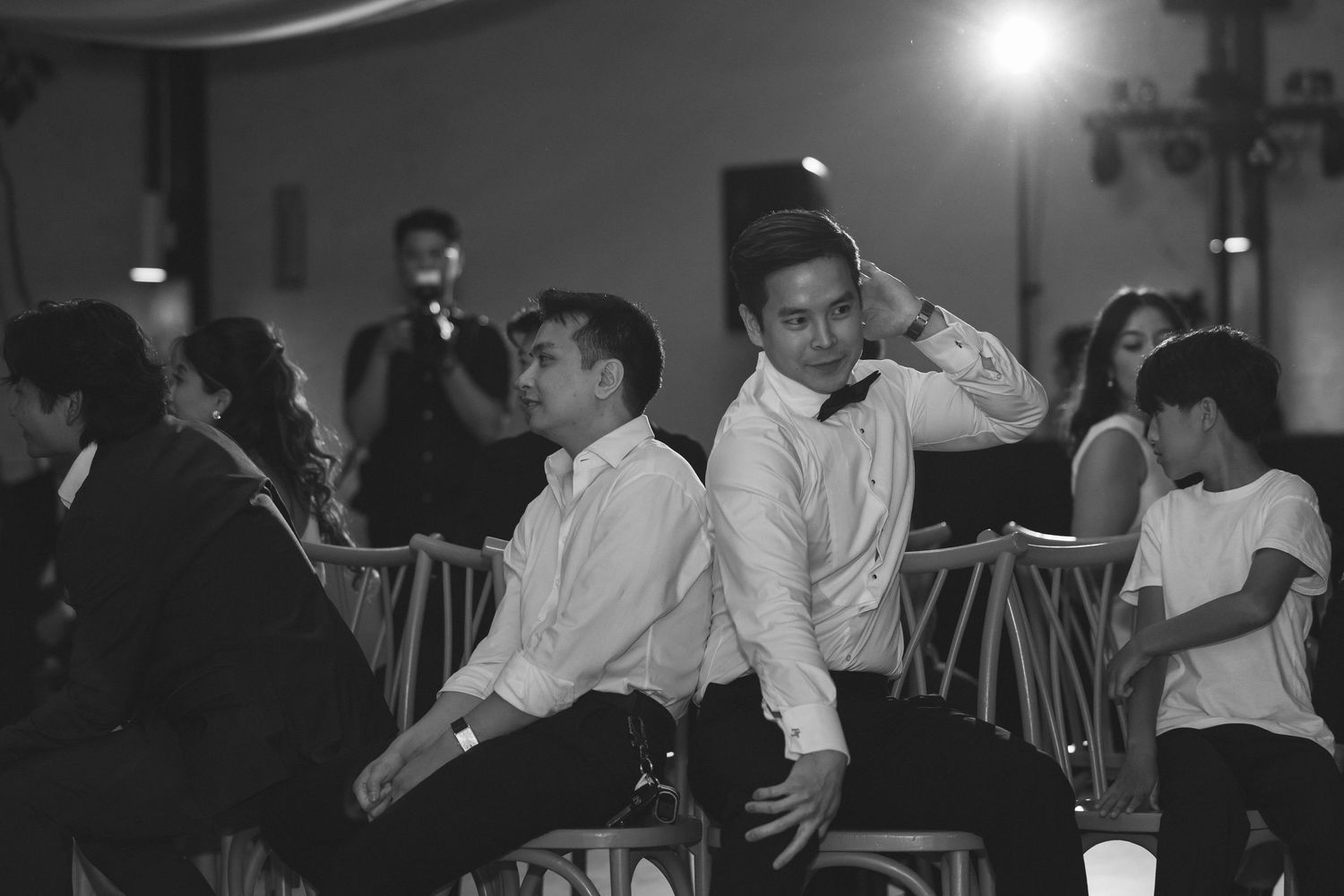 Black and white photo of wedding guests relaxing on chairs during reception celebration.