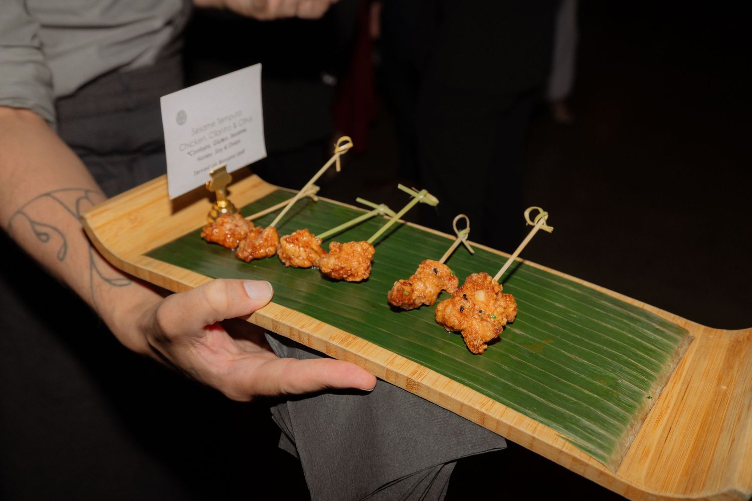 Elegant appetizers on bamboo skewers served on a green leaf-lined wooden tray at a catered event.