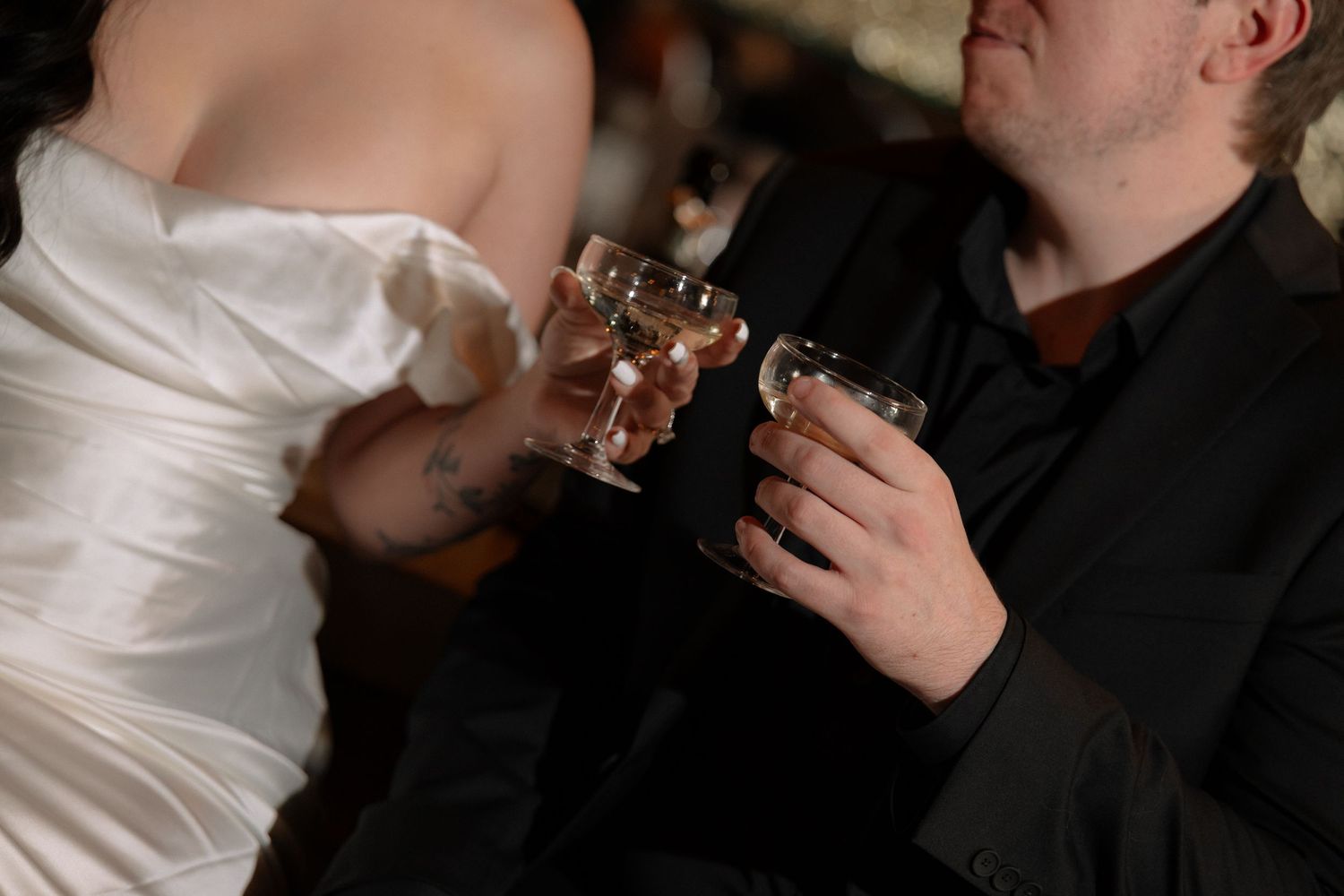 Bride and groom clinking glasses in a wedding toast, wearing white dress and black suit.
