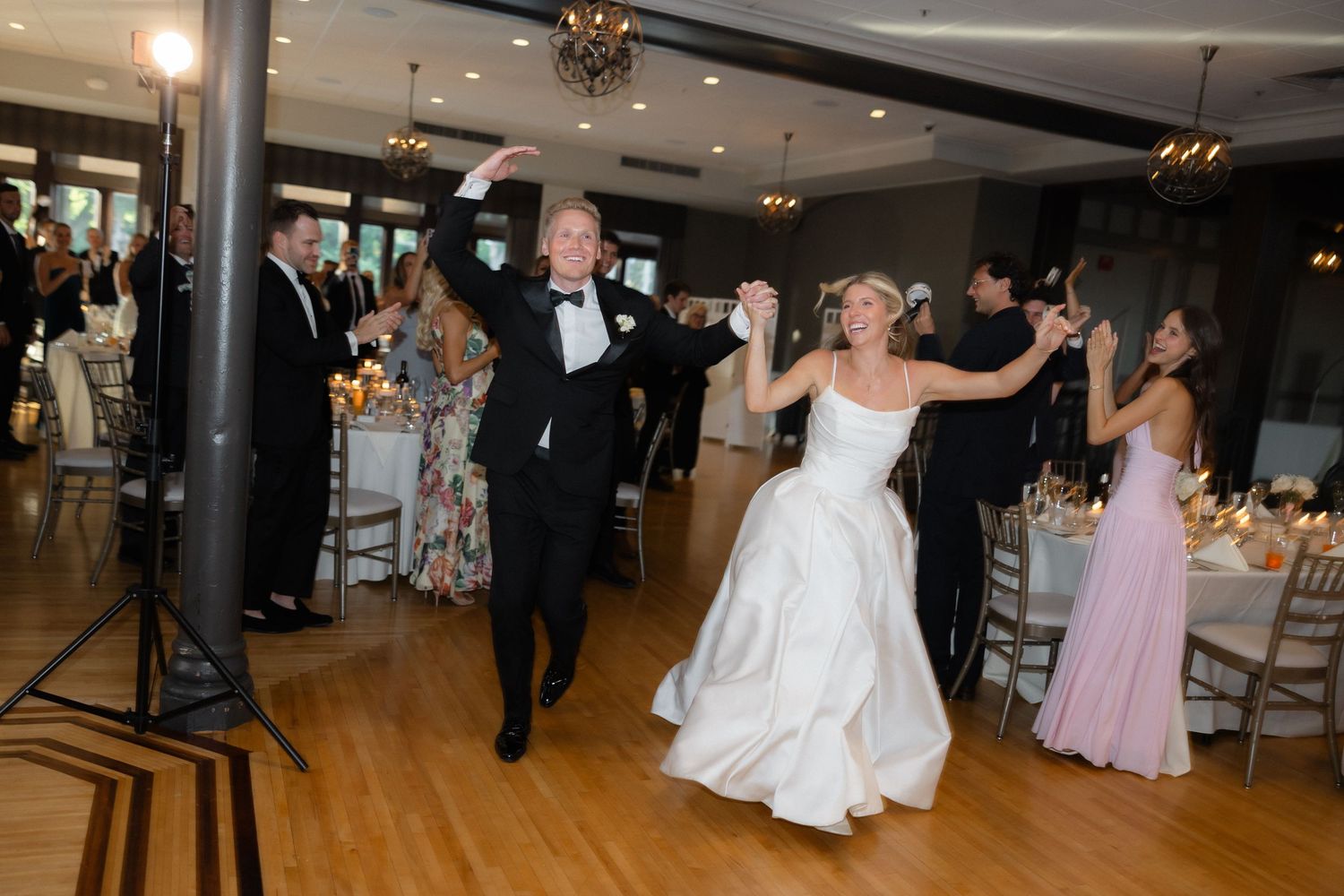 Bride in white gown and groom in tuxedo making grand entrance onto dance floor at wedding reception.