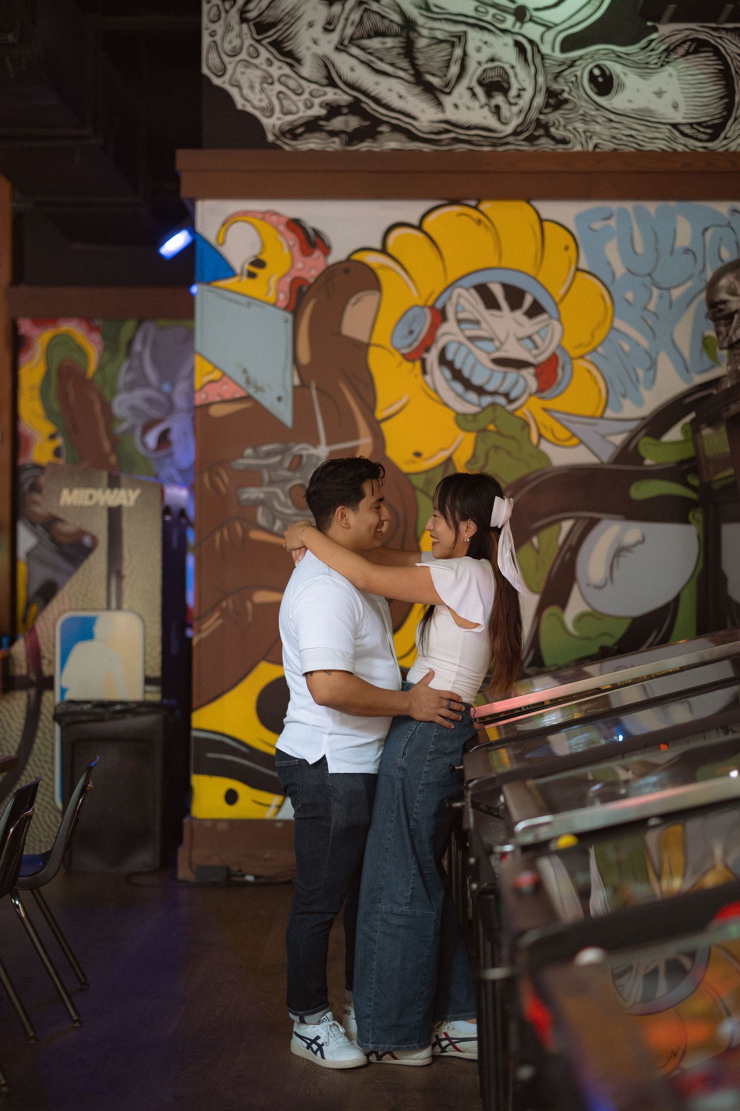 Couple embracing romantically in a colorful arcade with vibrant graffiti murals in the background.