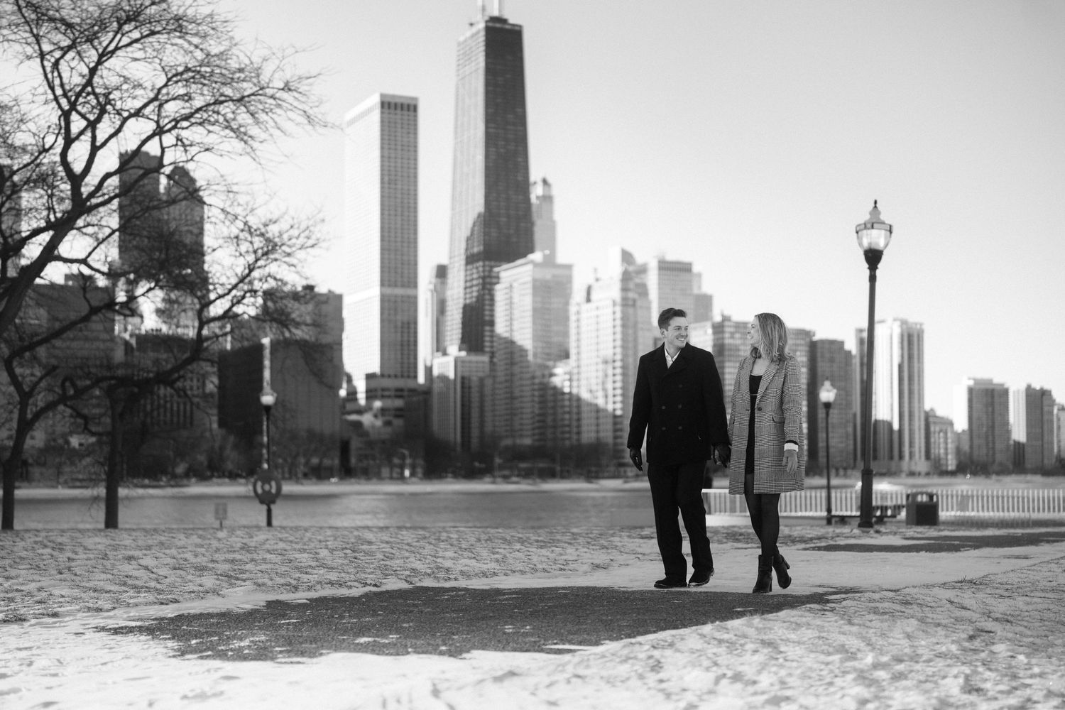 A couple walks along a snowy lakefront path with the Chicago skyline in the background.