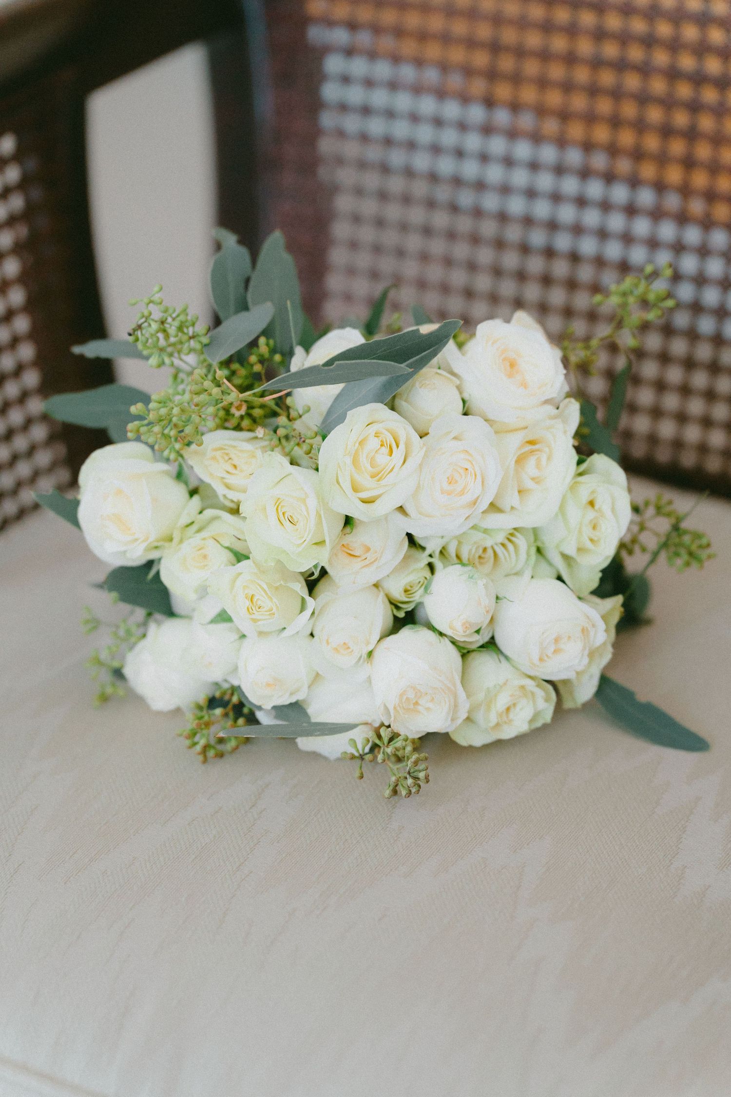 Elegant bridal bouquet of white roses and eucalyptus on a chair.