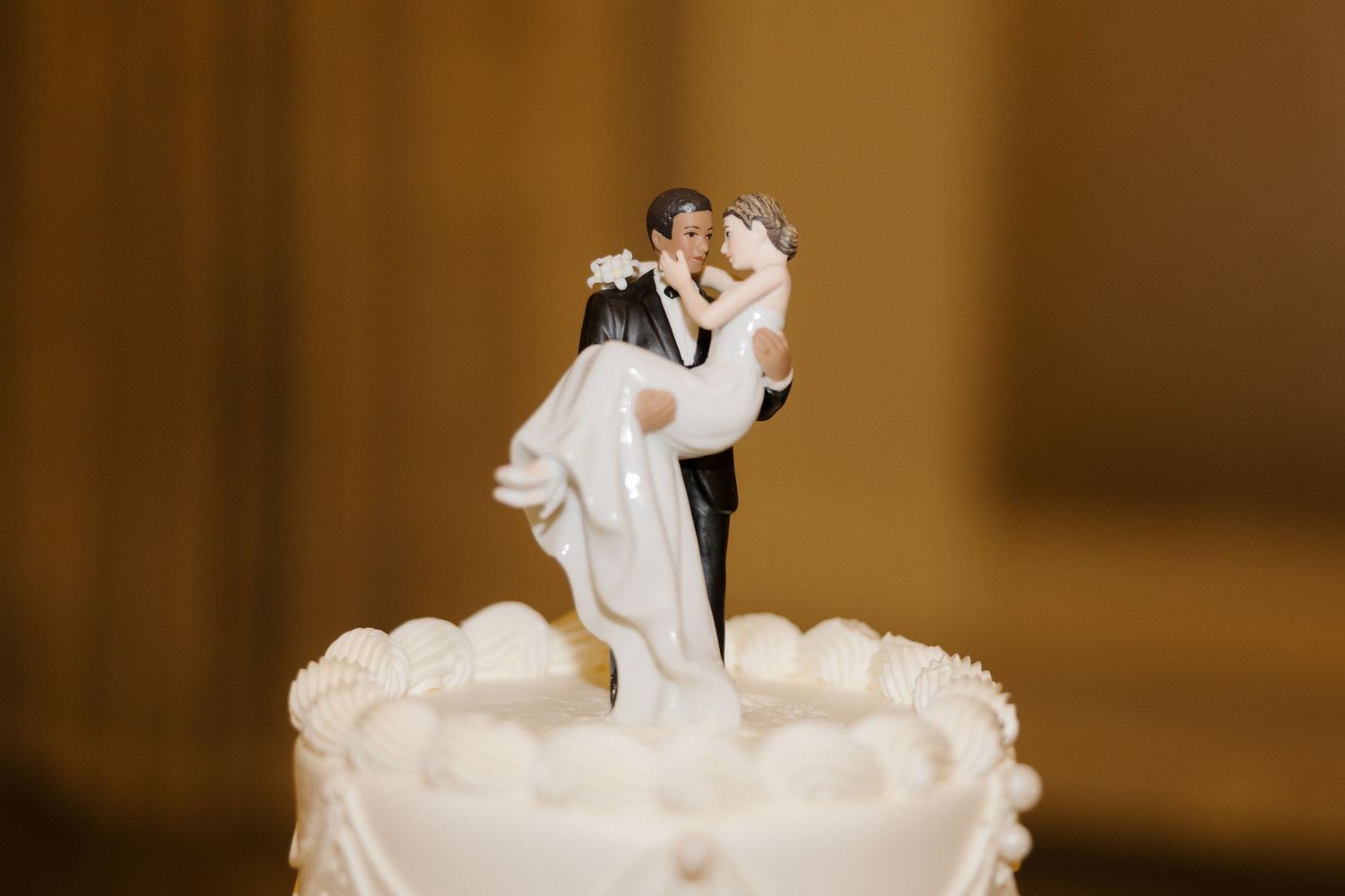 Classic wedding cake topper figurine of groom lifting bride in white dress on elegant white tiered cake.