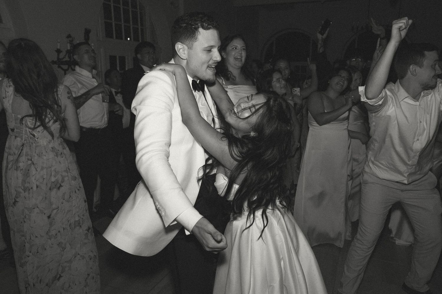 Bride and groom share energetic dance together at wedding reception, black and white photo.