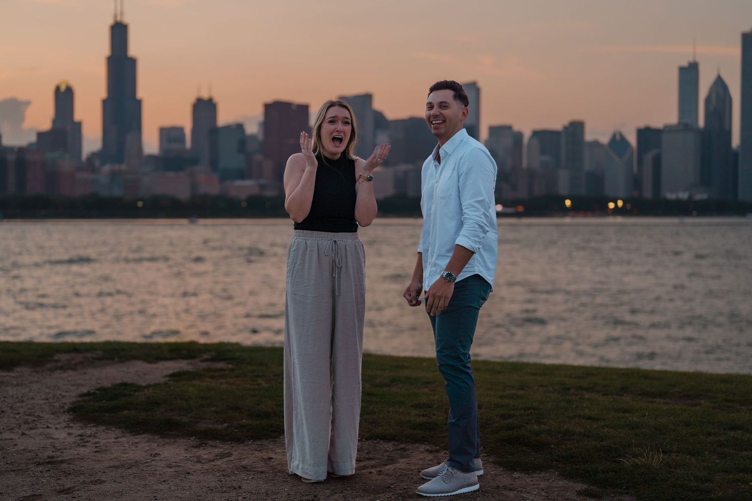 Excited woman reacting with joy as her partner smiles beside her against the Chicago skyline at dusk.