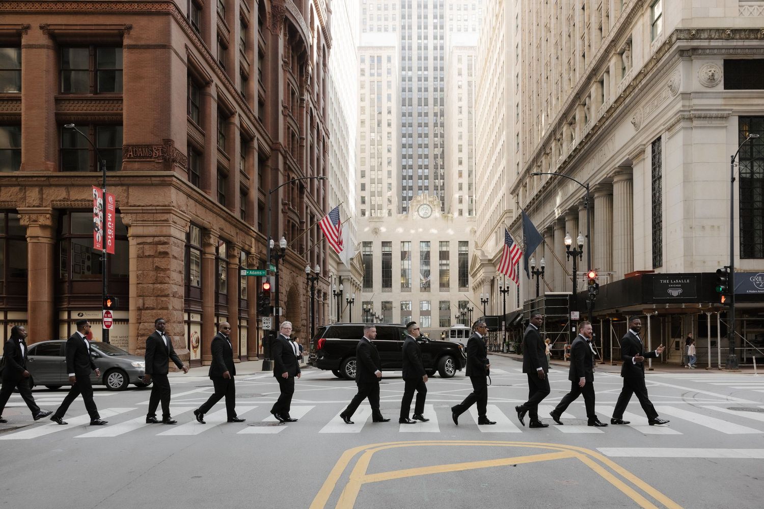 Business professionals in black suits crossing a busy urban intersection in downtown Chicago with American flags.
