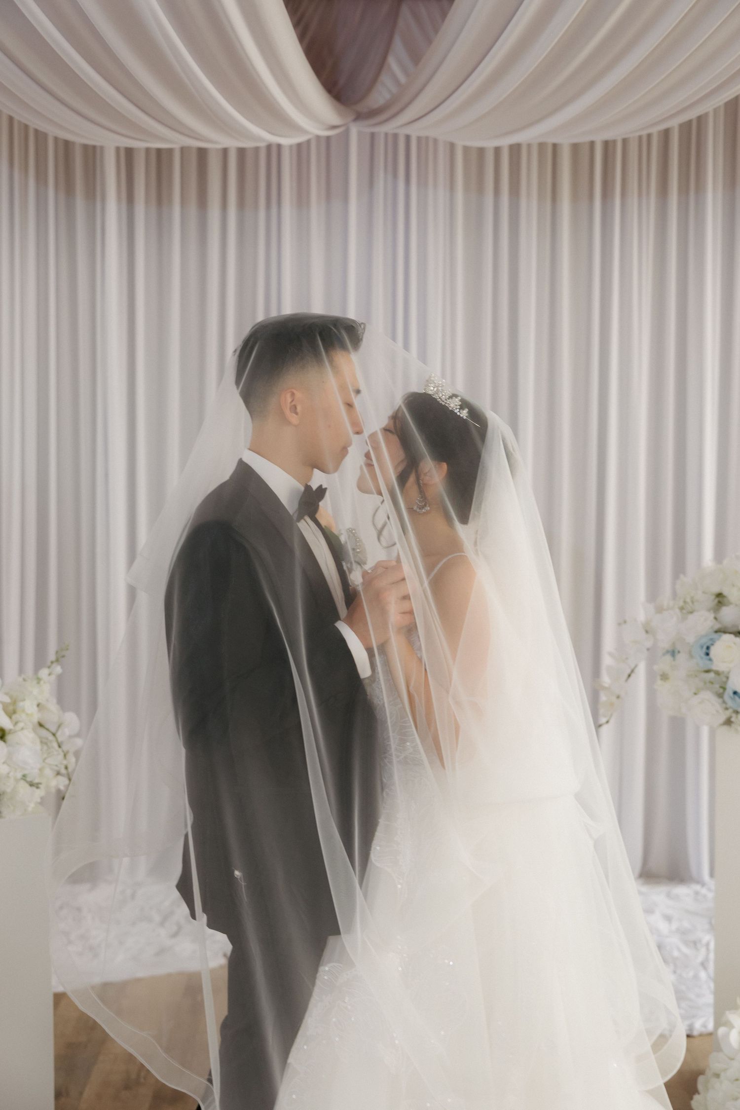 Bride and groom share an intimate kiss under a flowing white veil at elegant wedding ceremony.