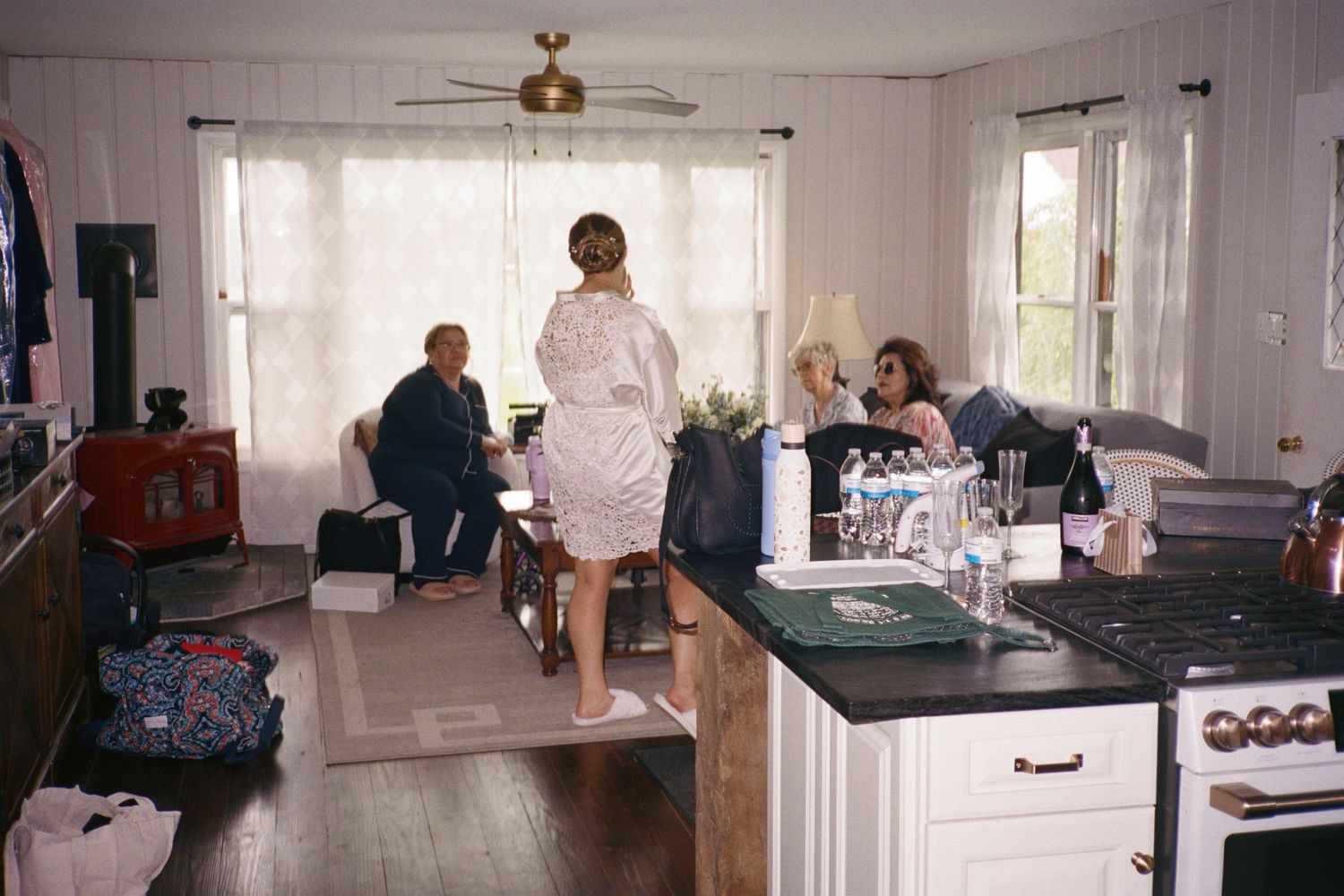 People gathering in a cozy home kitchen and living area, with a woman in a white robe standing near the counter.