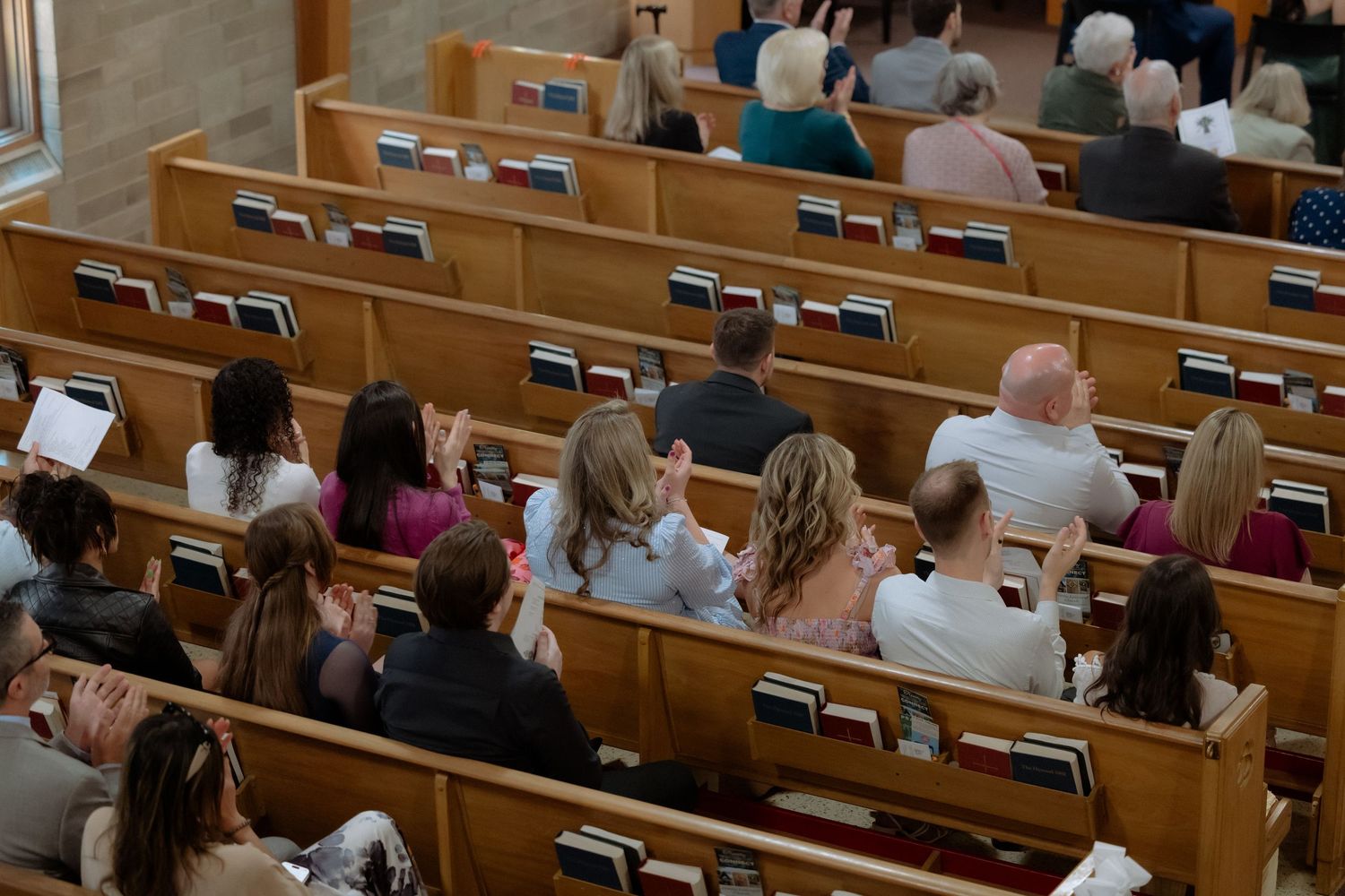 Congregation seated in wooden church pews during a religious service, viewed from above.
