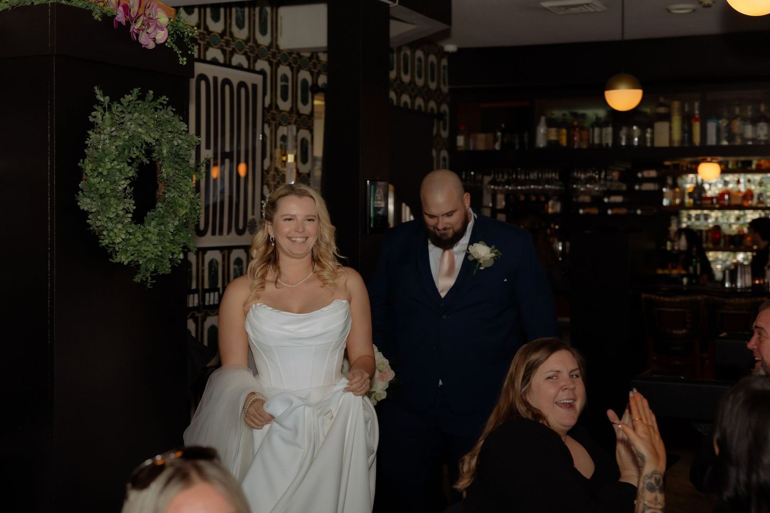 Bride and groom smiling as they enter their wedding reception at an elegant bar venue.