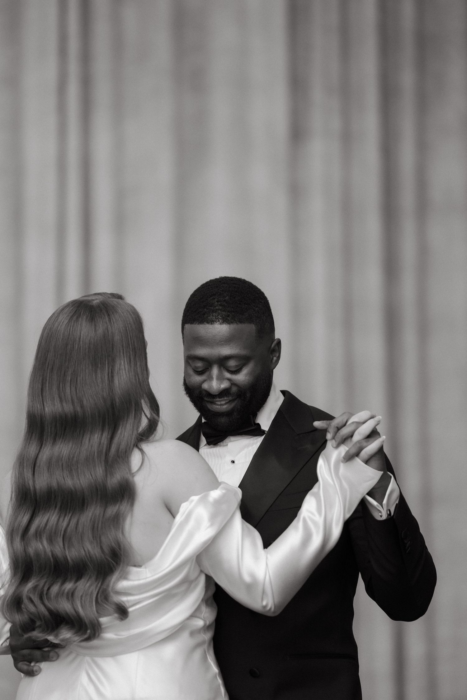 Black and white photo of an interracial couple sharing their first dance at a wedding reception.